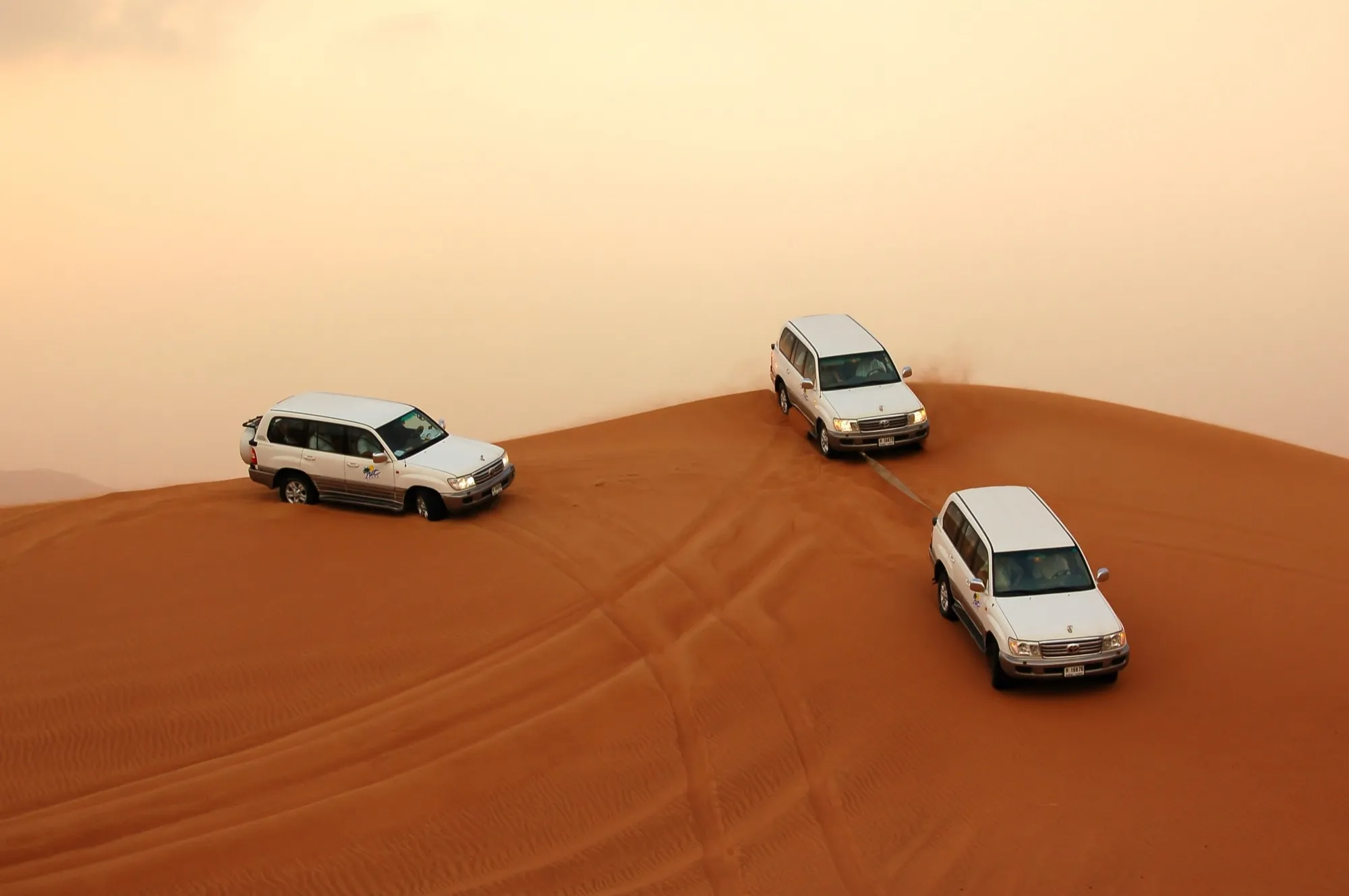 Three white Land Cruisers on the crest of a red dune during a desert drive near Dubai