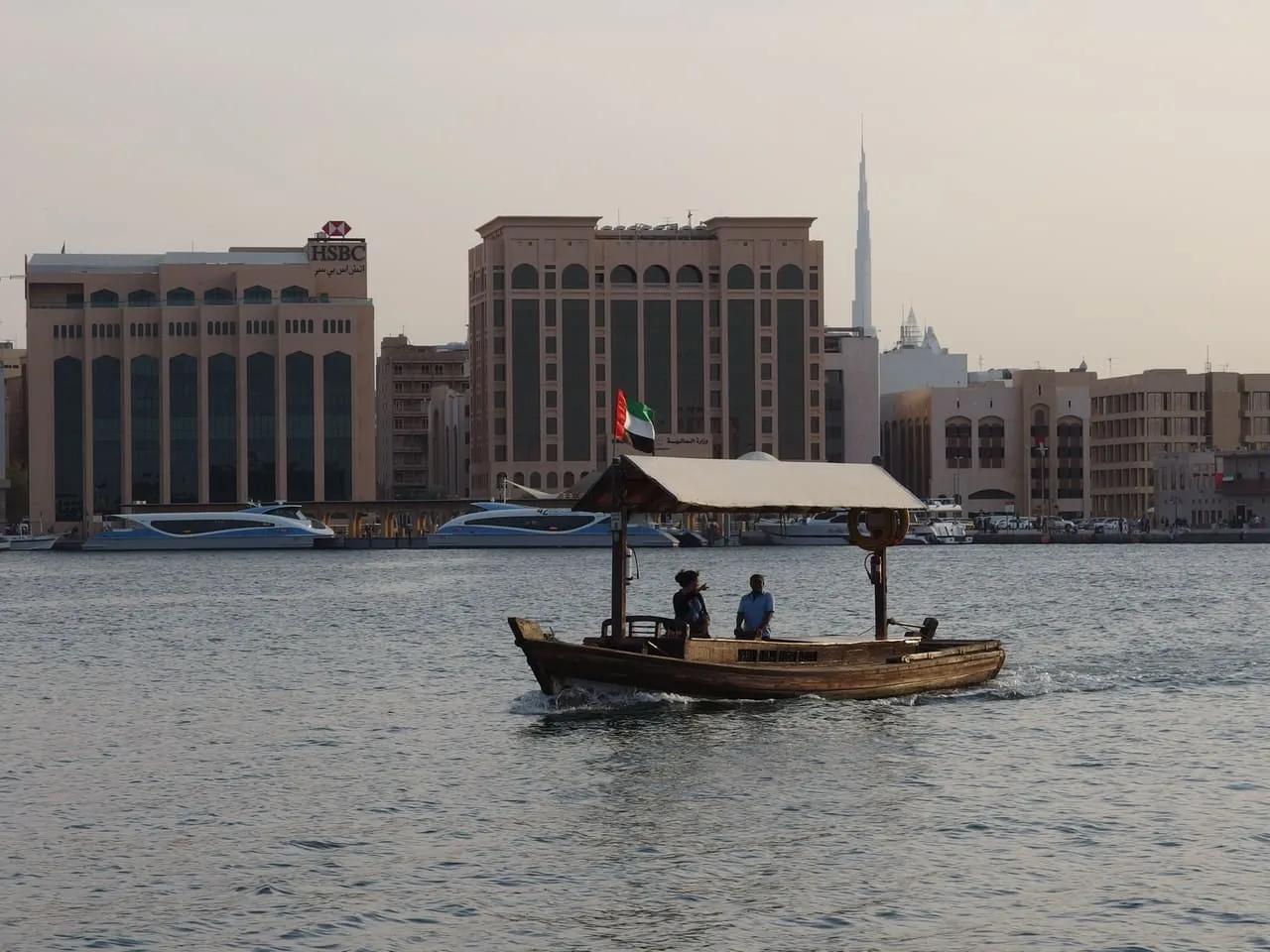 A wooden abra crossing Dubai Creek, with Burj Khalifa on the skyline behind