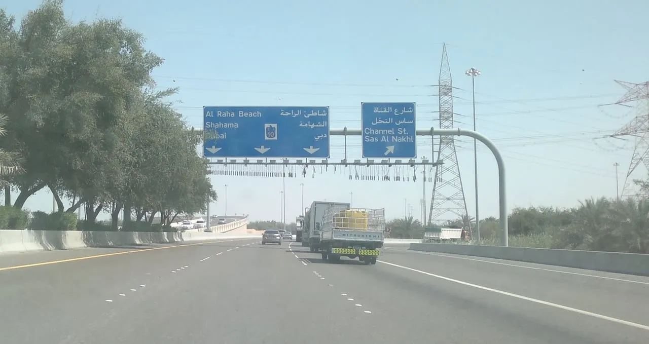 Overhead signs on a road in Abu Dhabi pointing ahead to Al Raha Beach, Shahama and Dubai