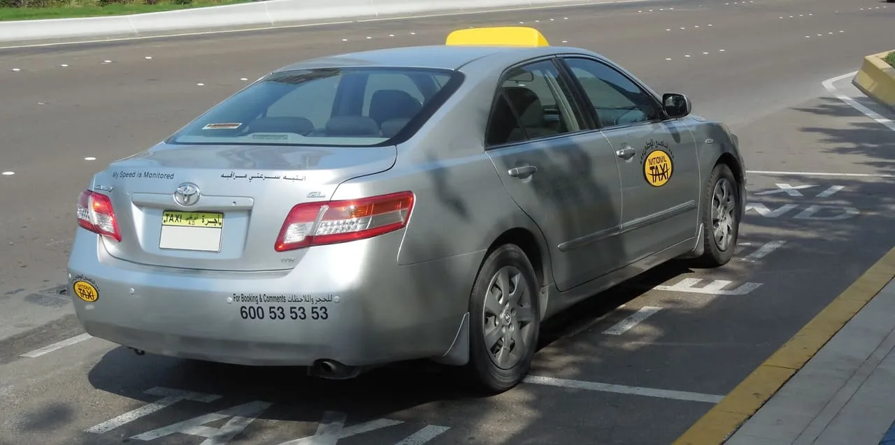 A silver Abu Dhabi taxi with a yellow roof sign, parked at the roadside