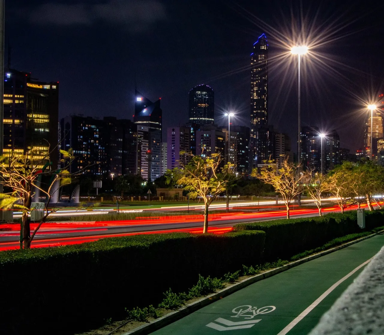 Abu Dhabi towers at night with light trails on the road and a green cycle lane in the foreground