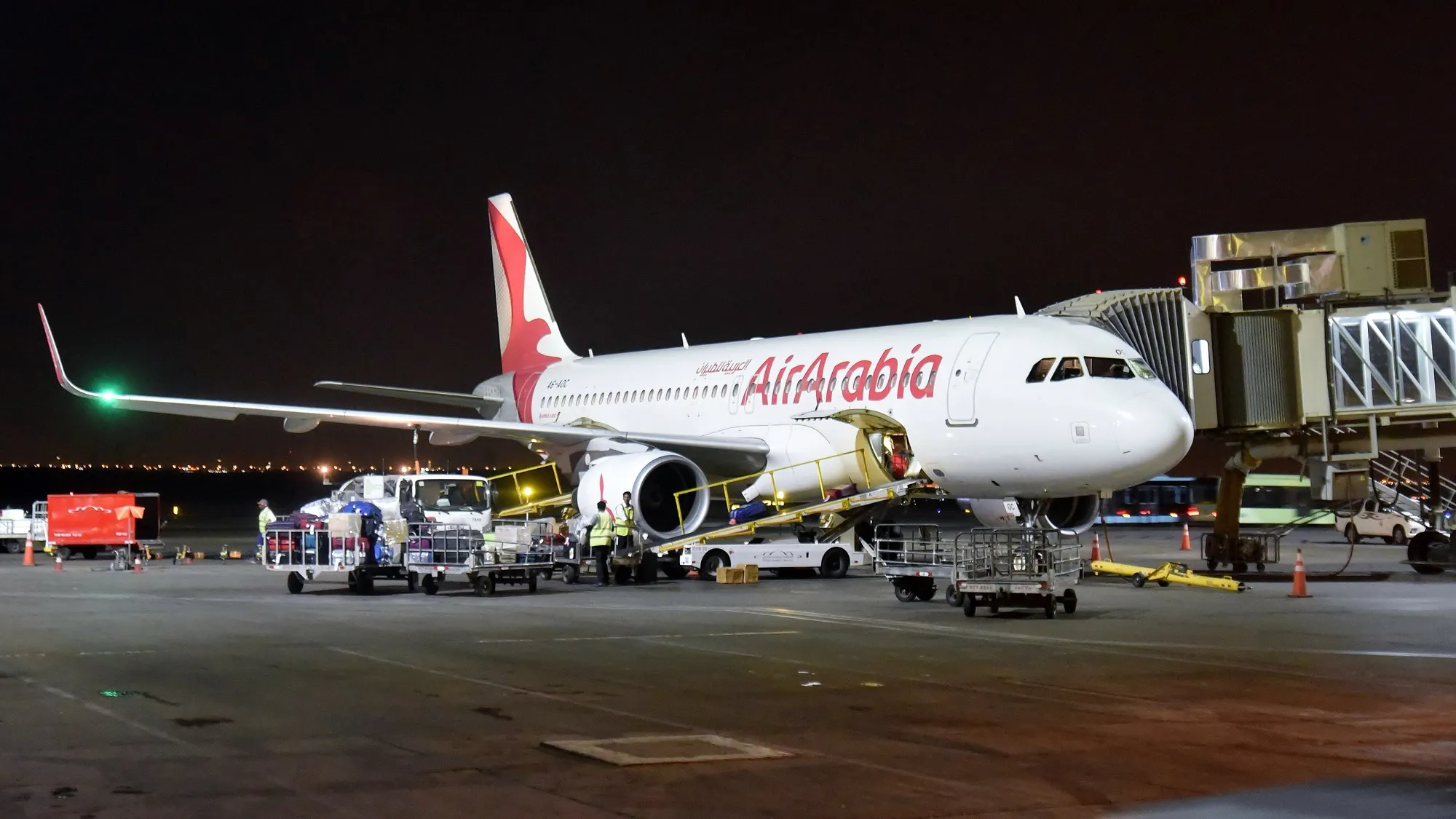 An Air Arabia Airbus A320 at a gate at Sharjah International Airport at night