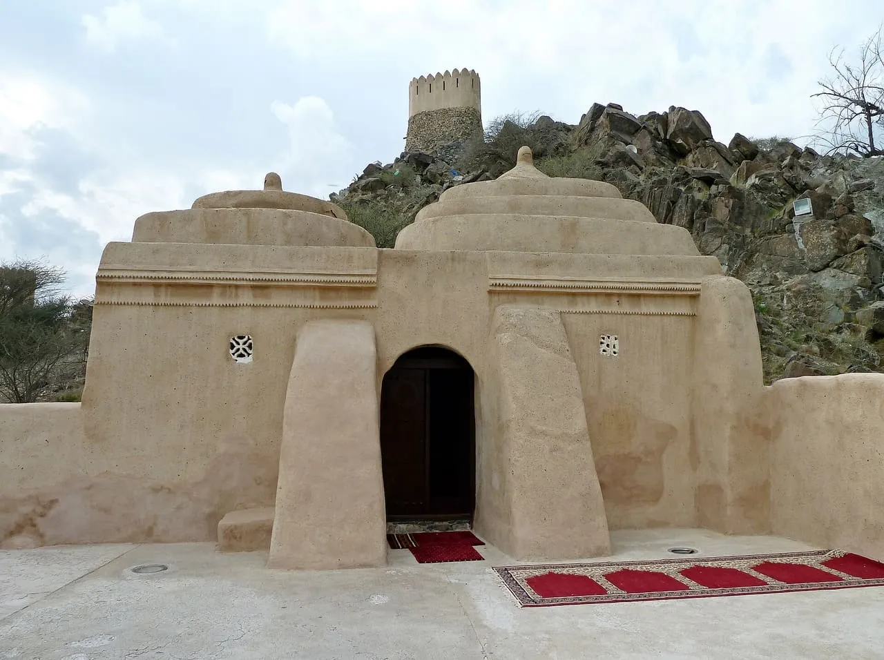 The domed mud and stone Al Bidya Mosque, with a watchtower on the rocky hill behind it