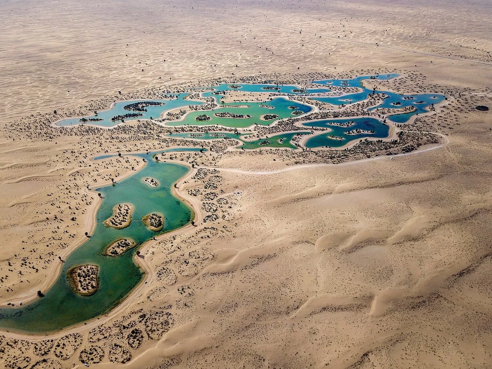 Aerial view of the man-made Al Qudra Lakes, green and blue pools set in pale desert sand