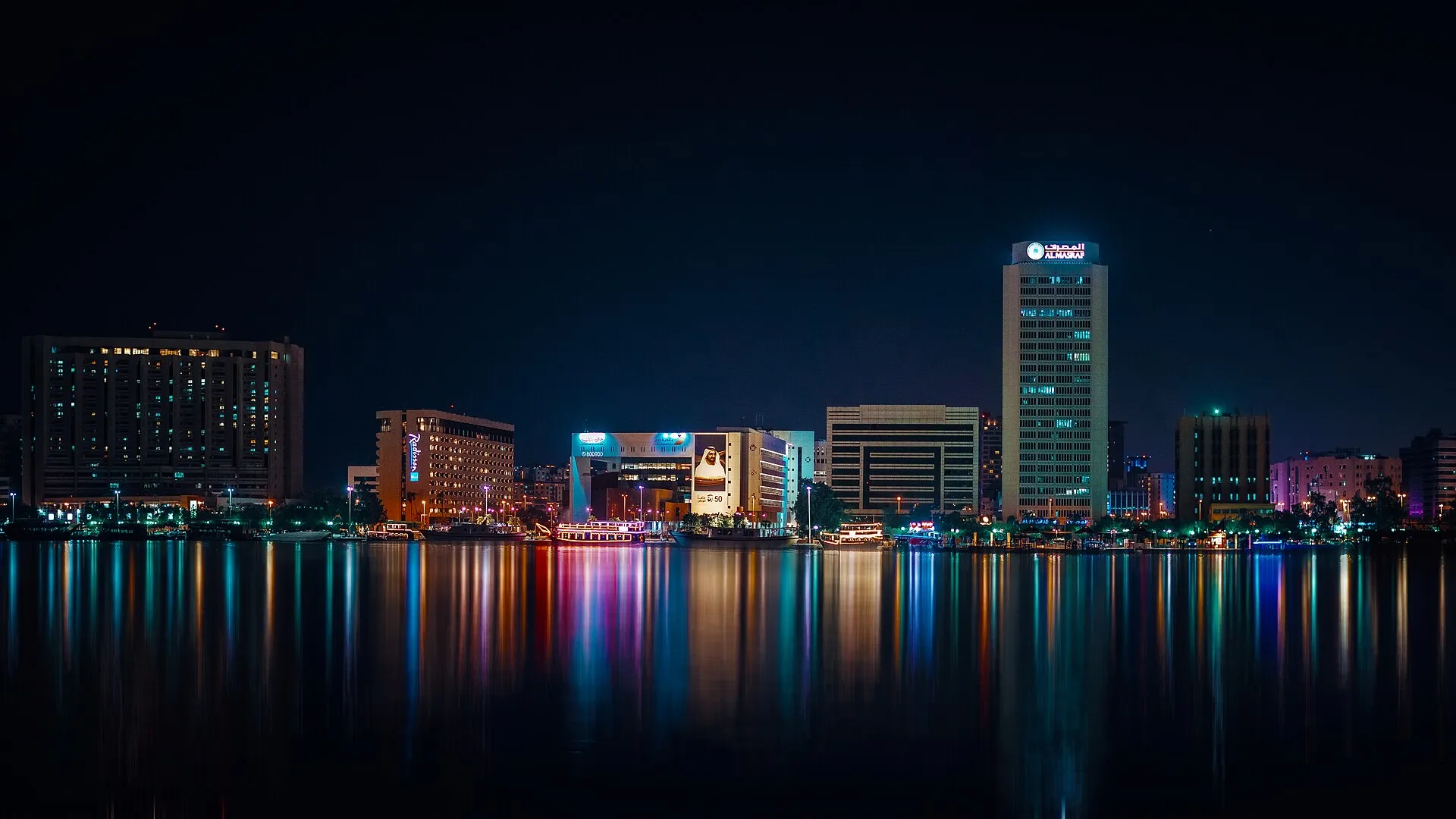 Buildings on the Deira side of Dubai Creek lit at night, reflected in the water