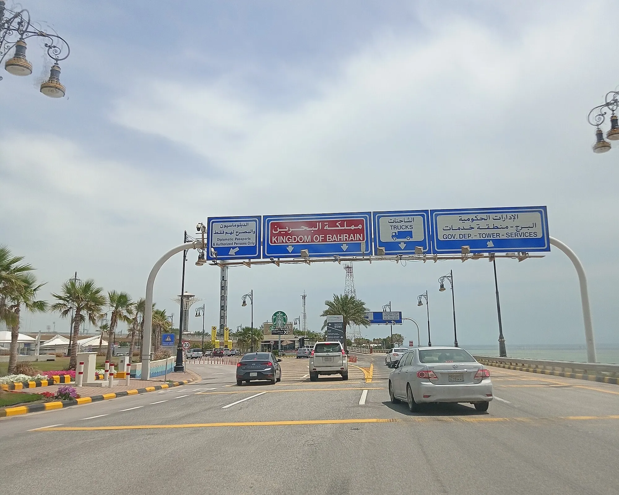 Cars approaching the Kingdom of Bahrain gantry signs on the causeway, with lanes marked for trucks and diplomatic passports