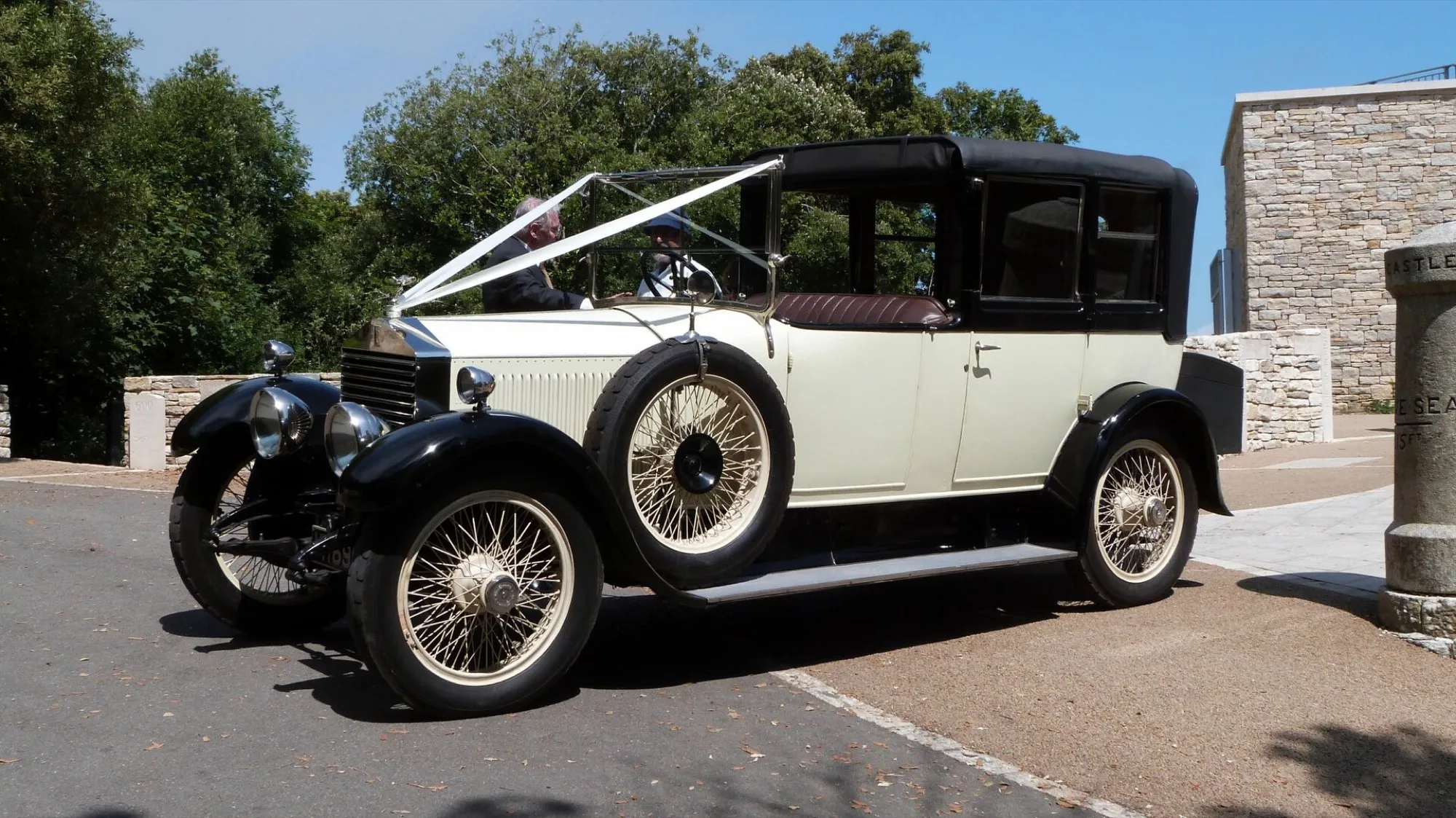 A cream and black 1926 Rolls-Royce 20hp Barker cabriolet with white ribbons on the bonnet, ready for a wedding