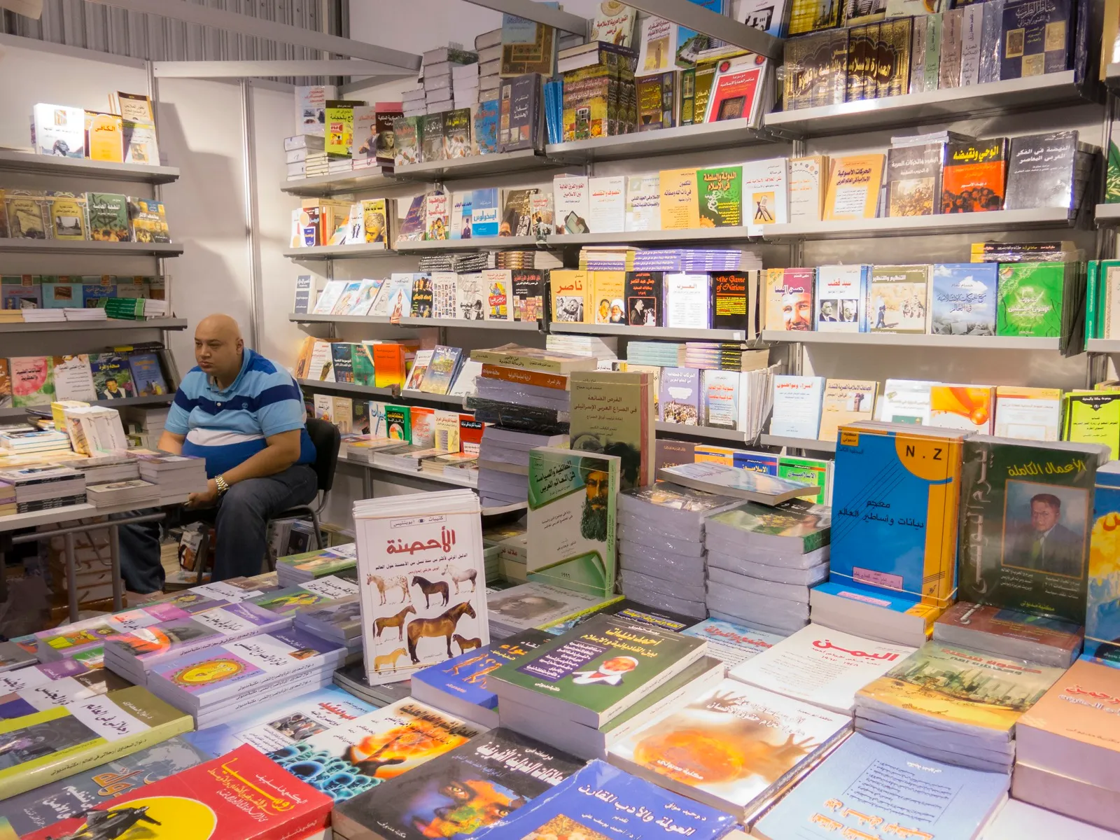 A publisher’s stall at the Sharjah International Book Fair, with shelves and tables stacked with Arabic books