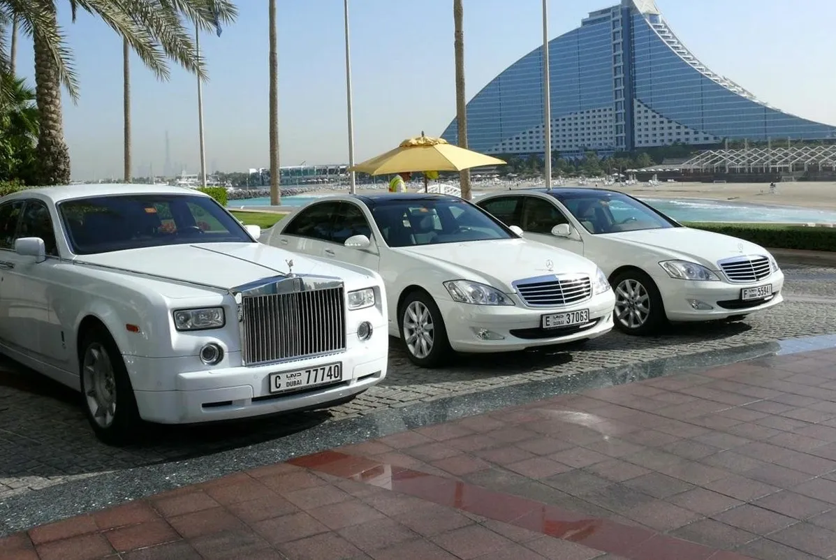 A white Rolls-Royce Phantom and two white Mercedes-Benz S-Class saloons parked at a Dubai beach hotel