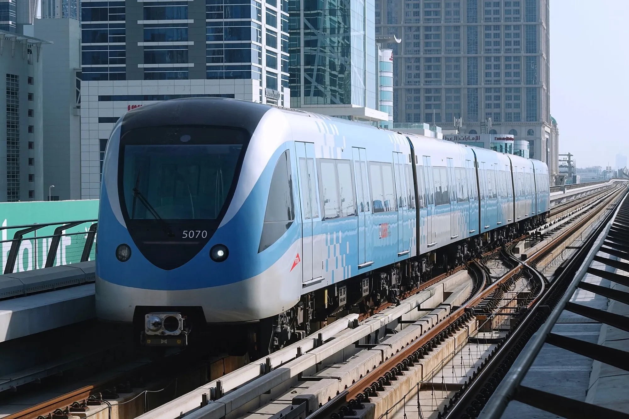 A blue and silver Dubai Metro train, number 5070, entering Business Bay station on the raised line