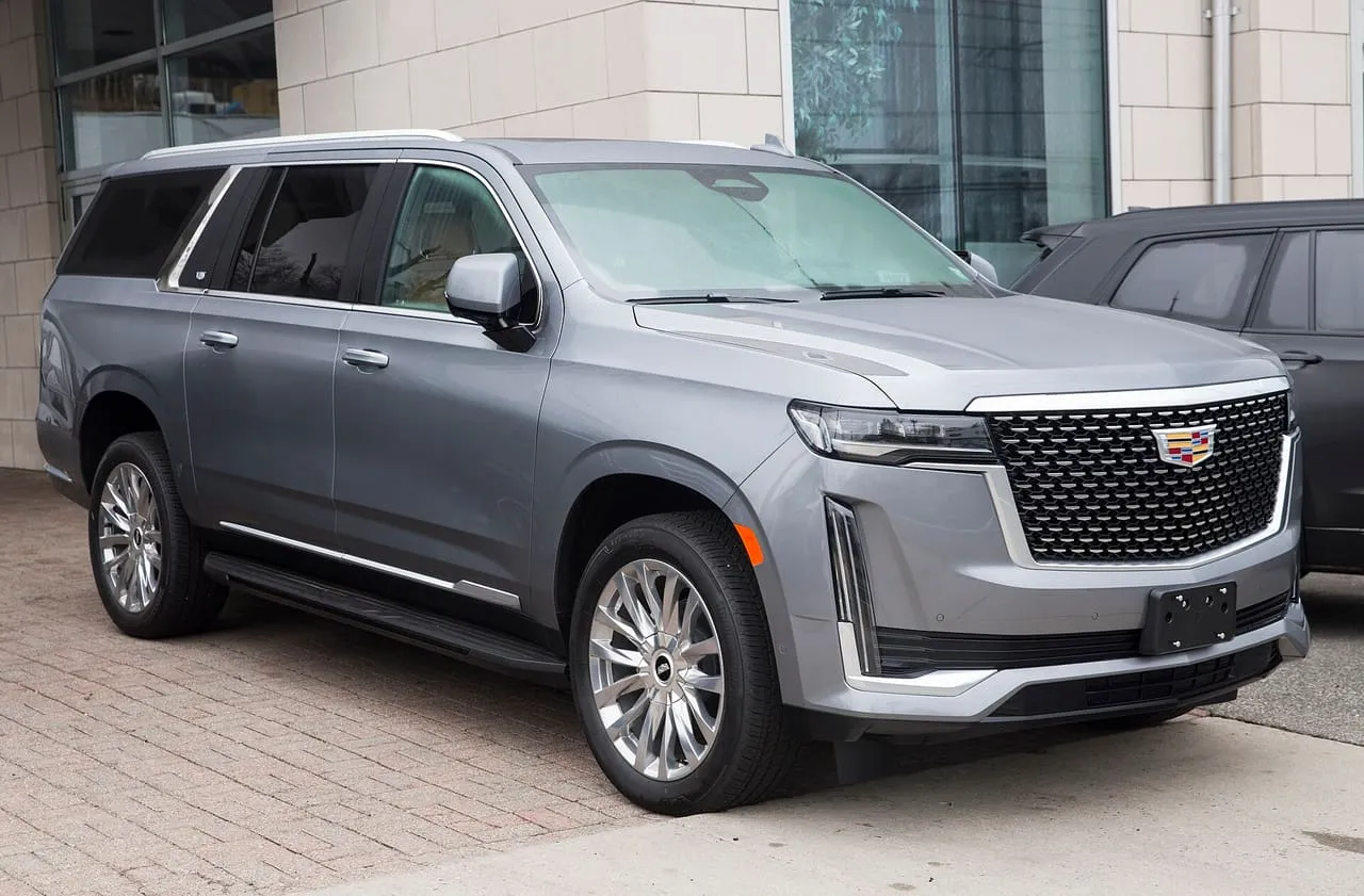 A silver Cadillac Escalade ESV SUV parked outside a building, seen from the front right