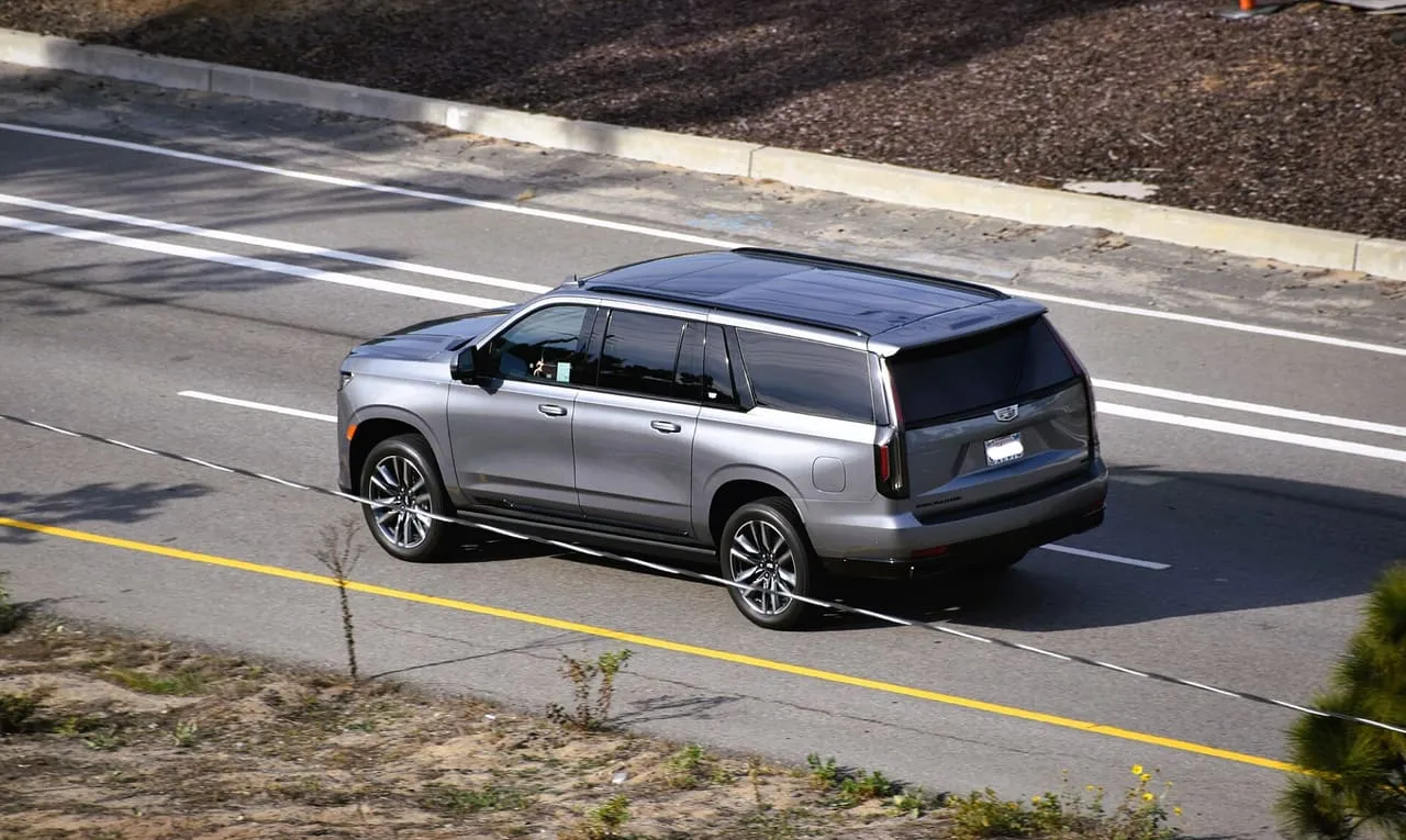 A silver Cadillac Escalade ESV on a highway, seen from above, showing its long rear section