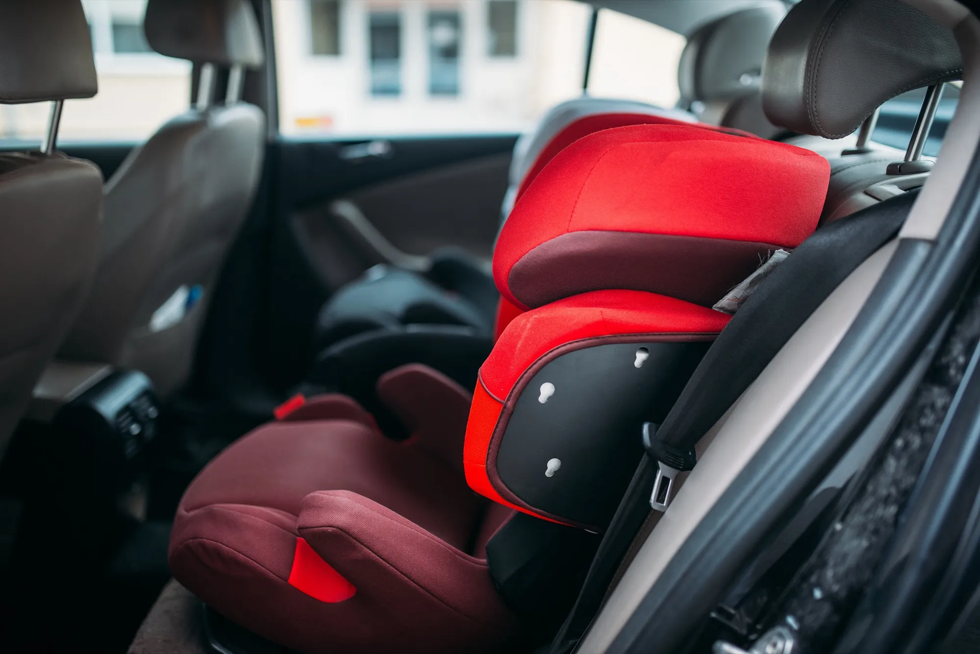 A red child booster seat fitted on the rear seat of a car