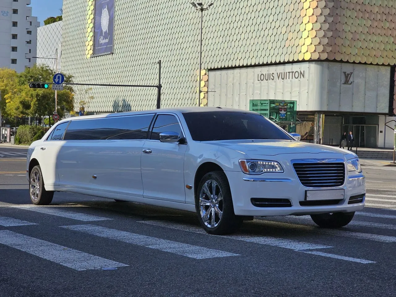 A white Chrysler 300 stretch limousine crossing a city road, its lengthened body sitting at sedan height