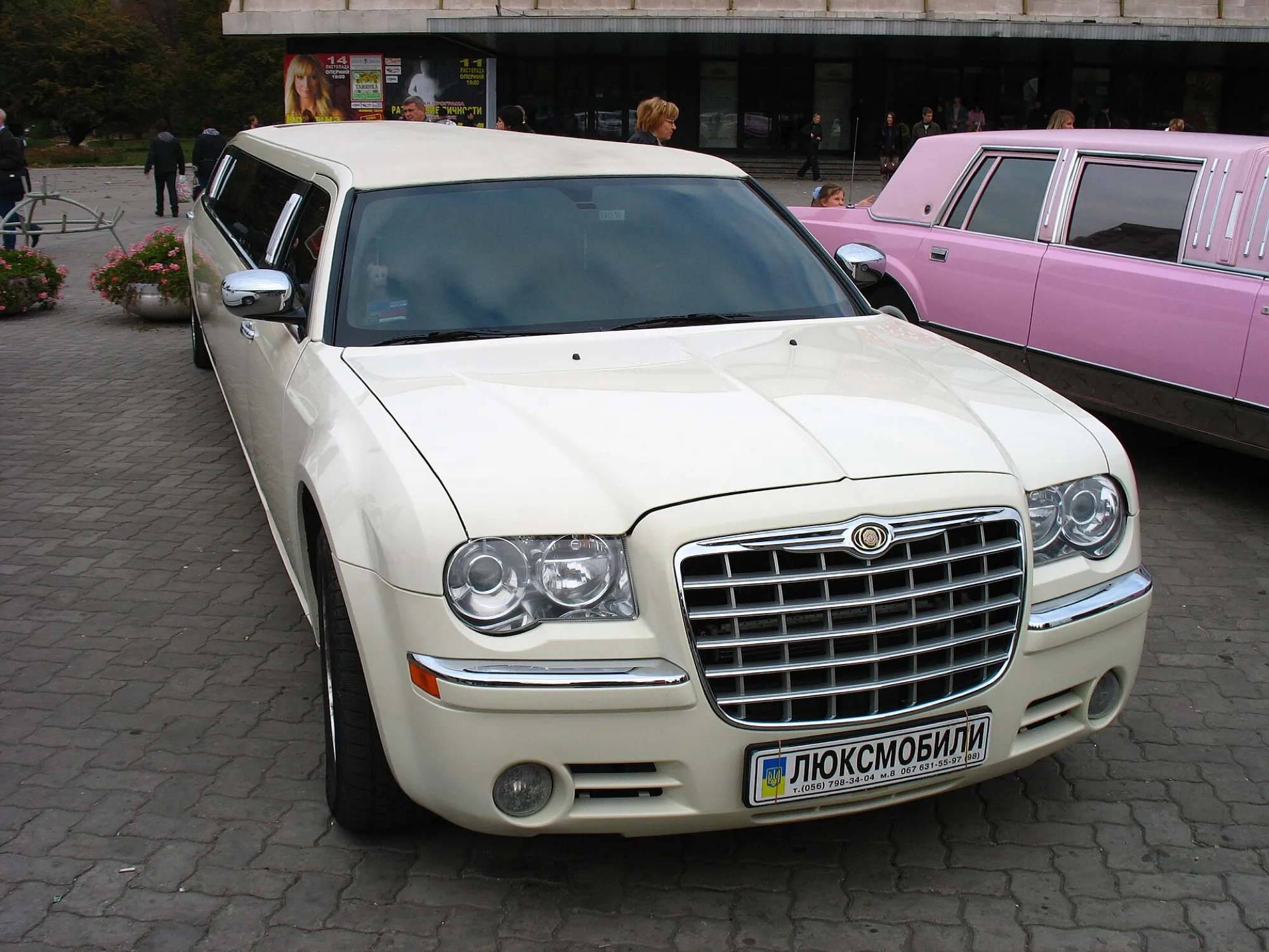 A cream Chrysler 300 stretch limousine parked beside a pink stretch limousine