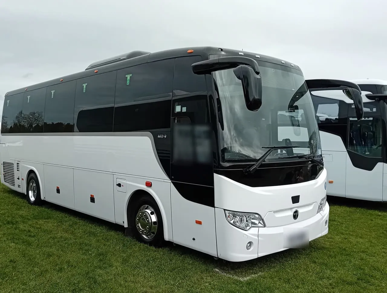White midi coach parked on grass, a representative image of the 35-seat coach size; the partner's coach may be a different make