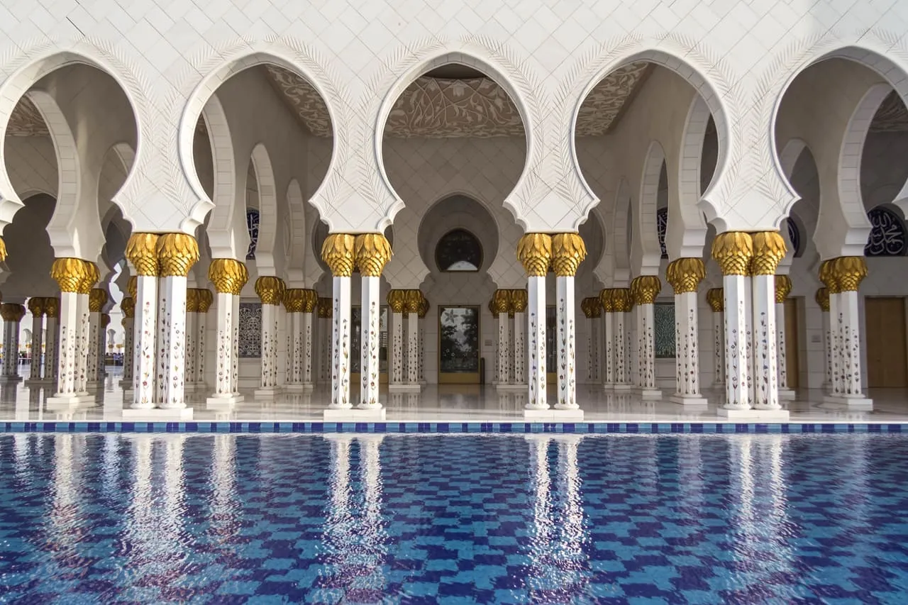 Gold-topped columns of the Sheikh Zayed Grand Mosque colonnade reflected in a blue-tiled pool