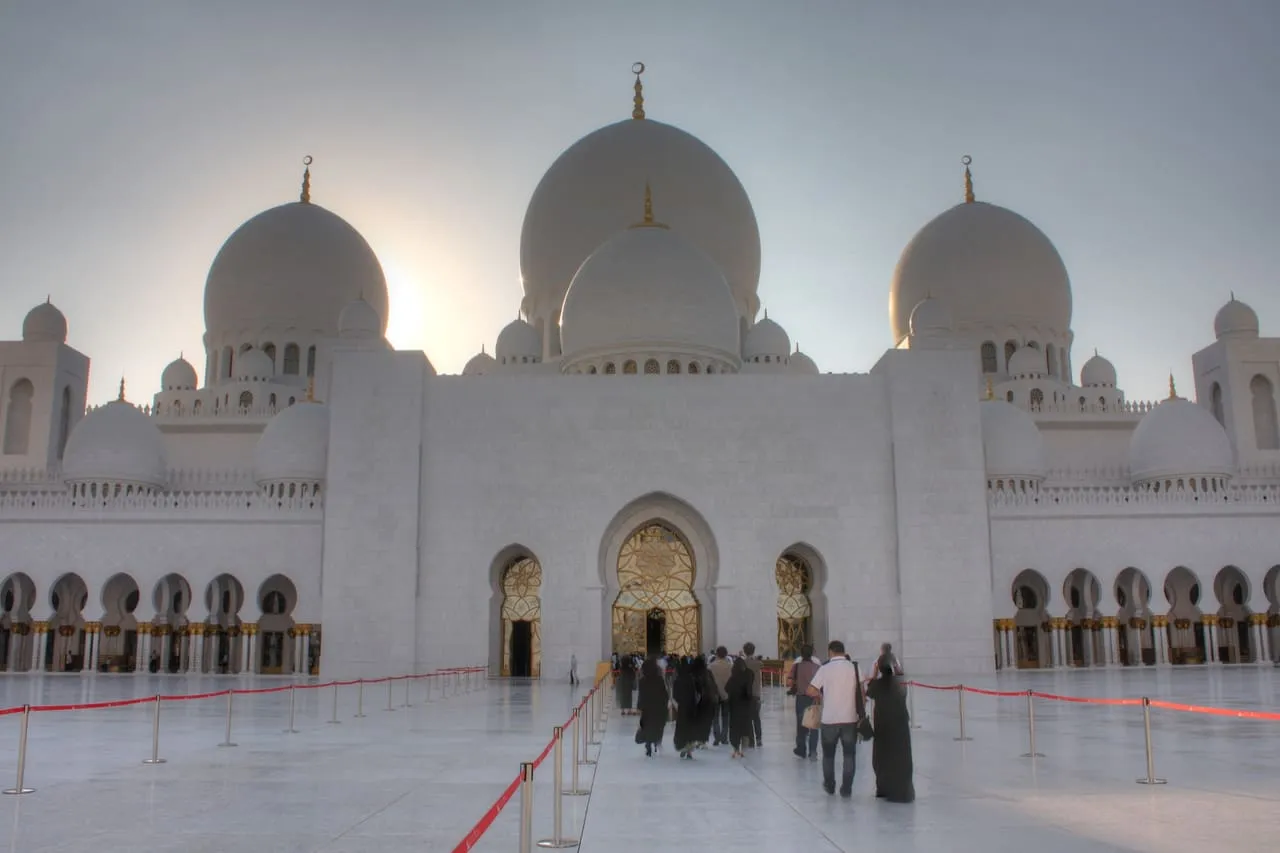 Visitors crossing the marble courtyard towards the main prayer hall entrance of the Sheikh Zayed Grand Mosque