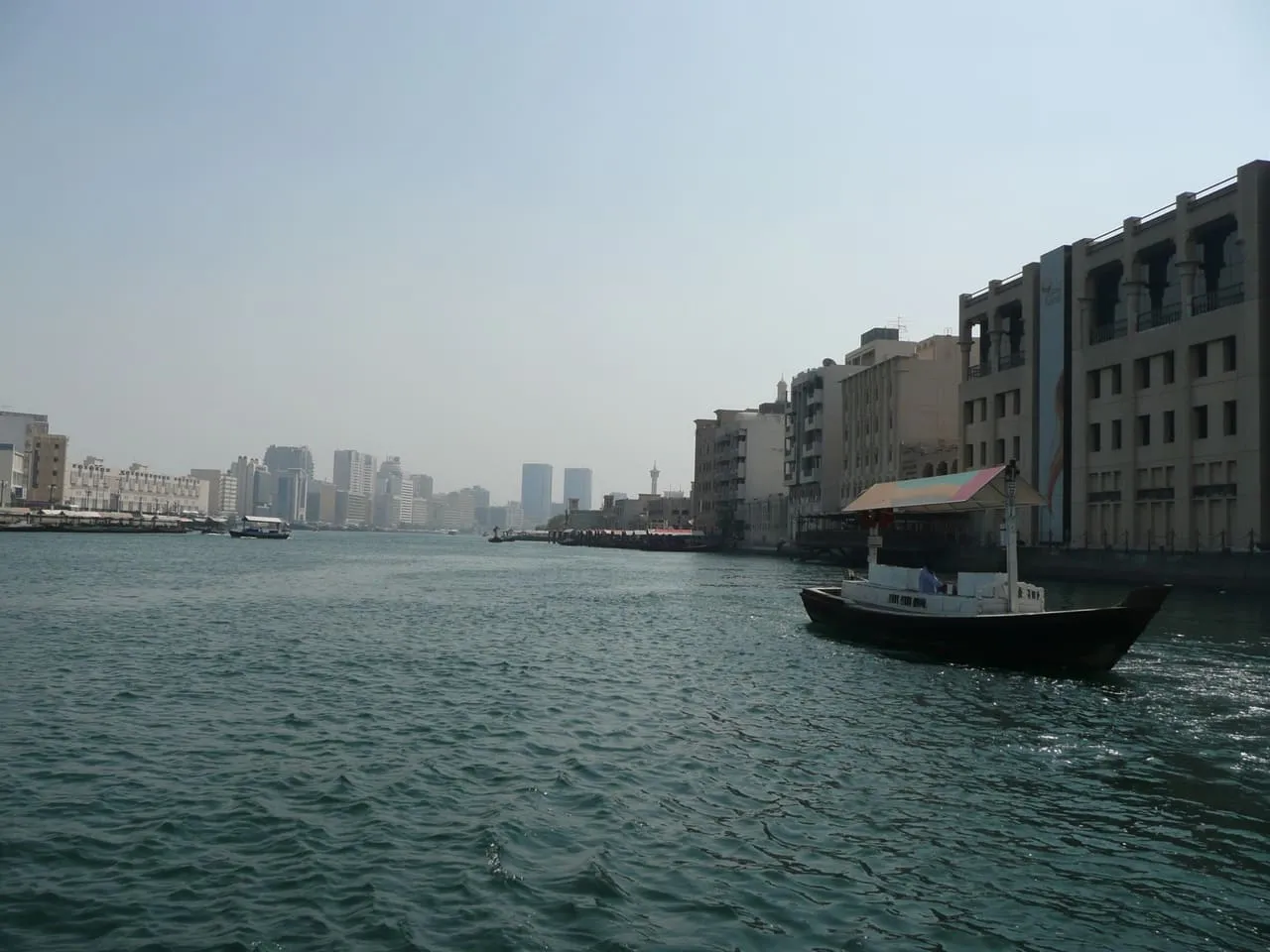 A traditional abra boat crossing Dubai Creek with old Deira buildings on the bank