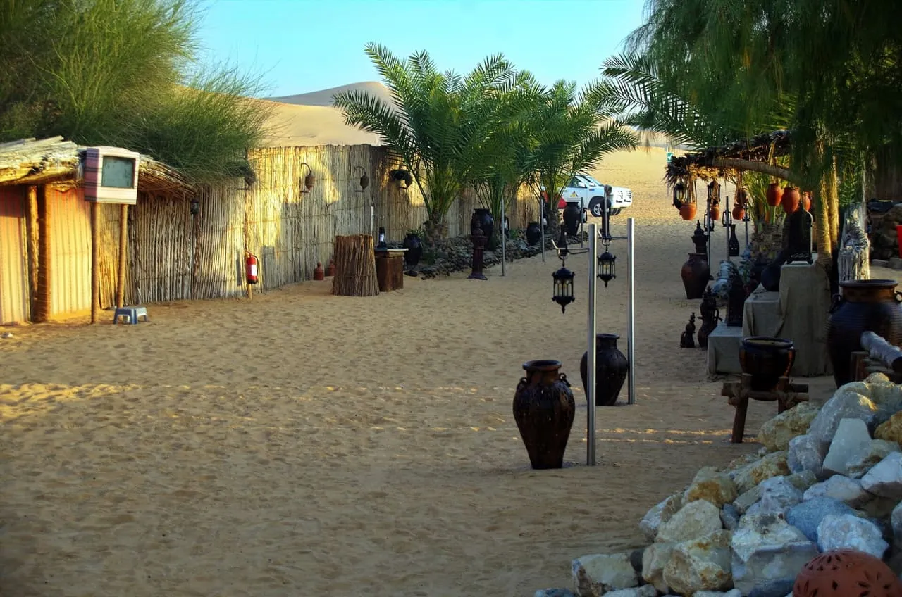 Palm trees, palm-frond huts and clay pots along a sandy path at a desert camp in the dunes of Dubai