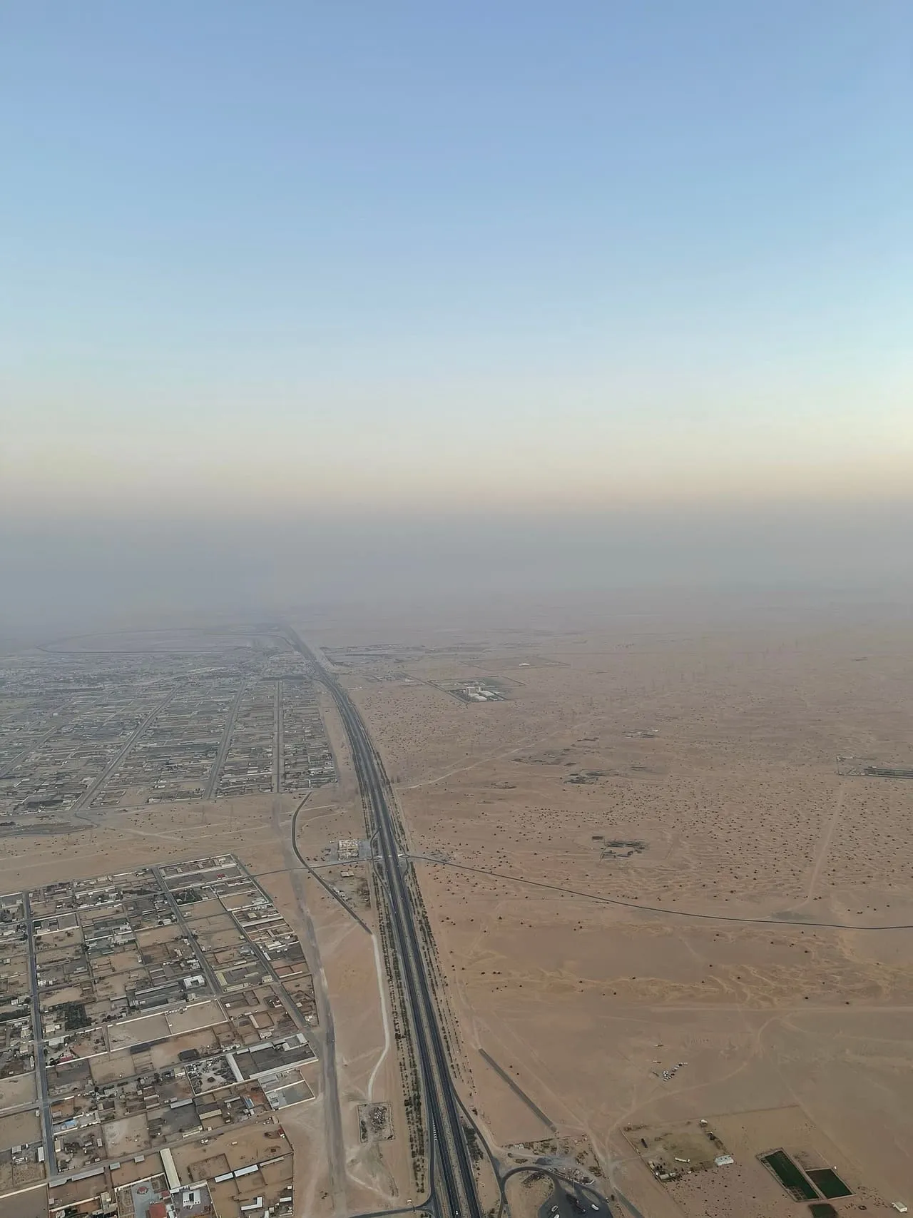 Aerial view of a highway running between Dubai's outer suburbs and the open desert in the morning haze