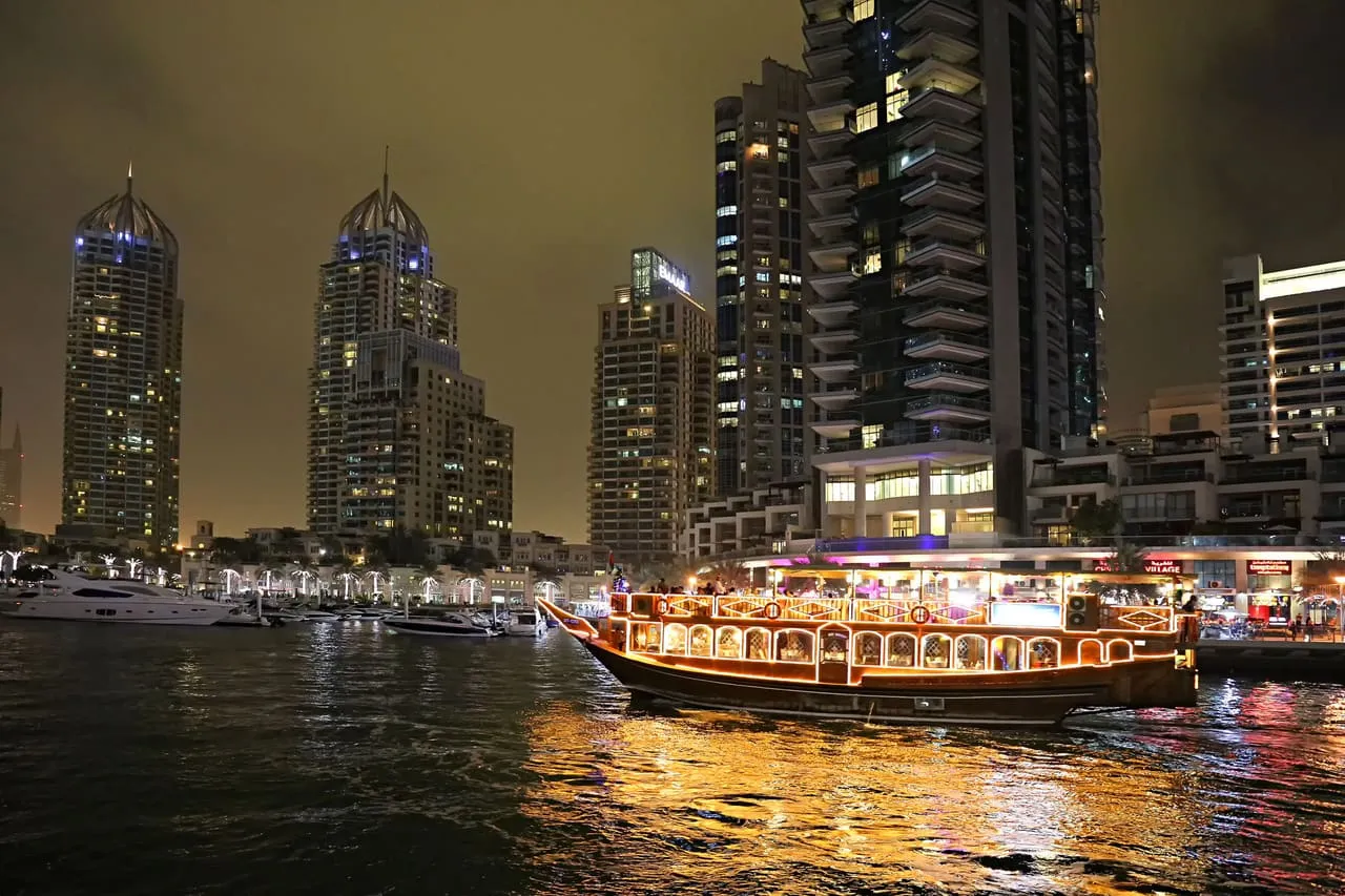 A lit dinner dhow cruising the Dubai Marina canal at night, past the residential towers