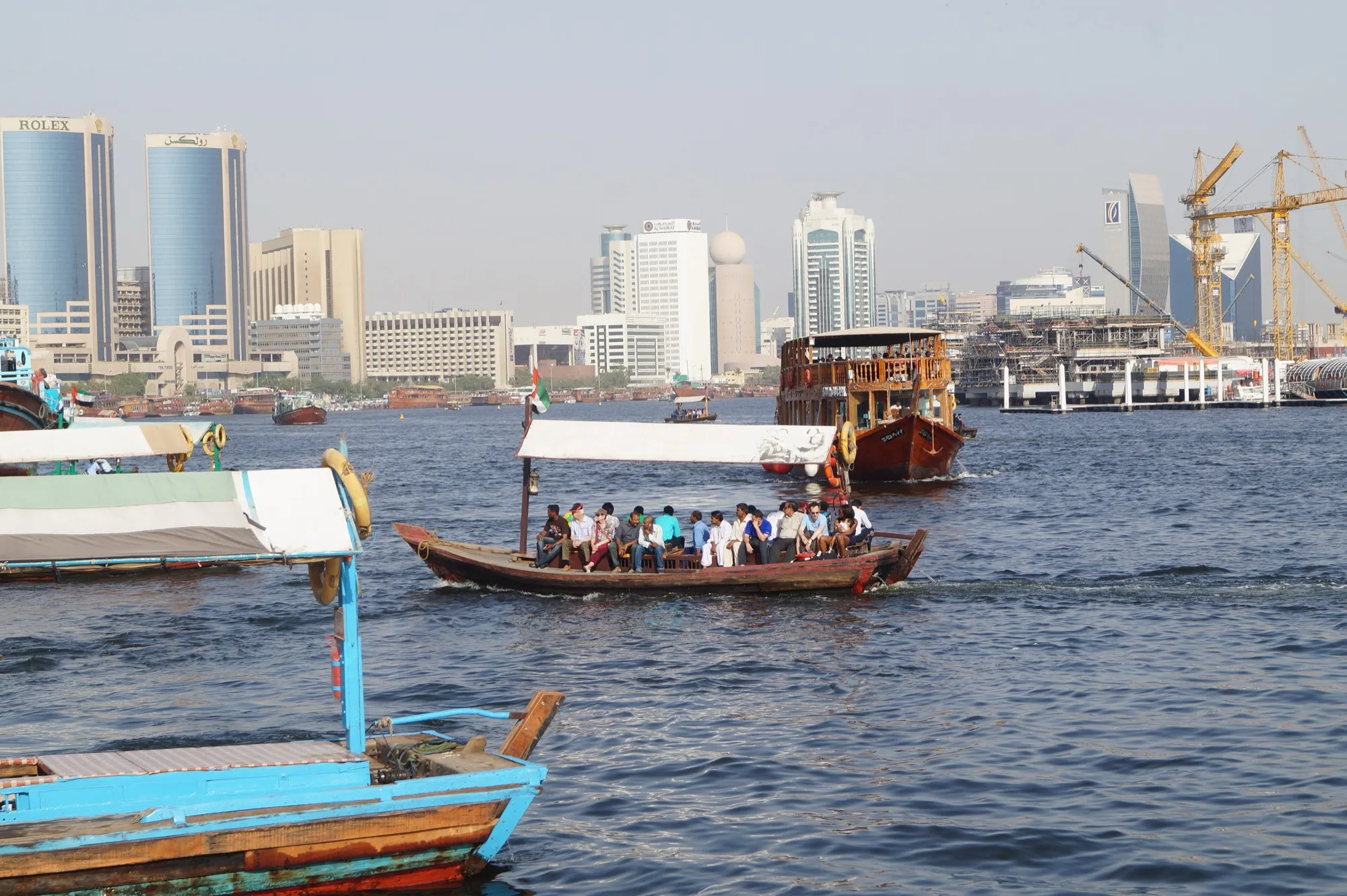 An abra water taxi crossing Dubai Creek with dhows and the Deira skyline behind