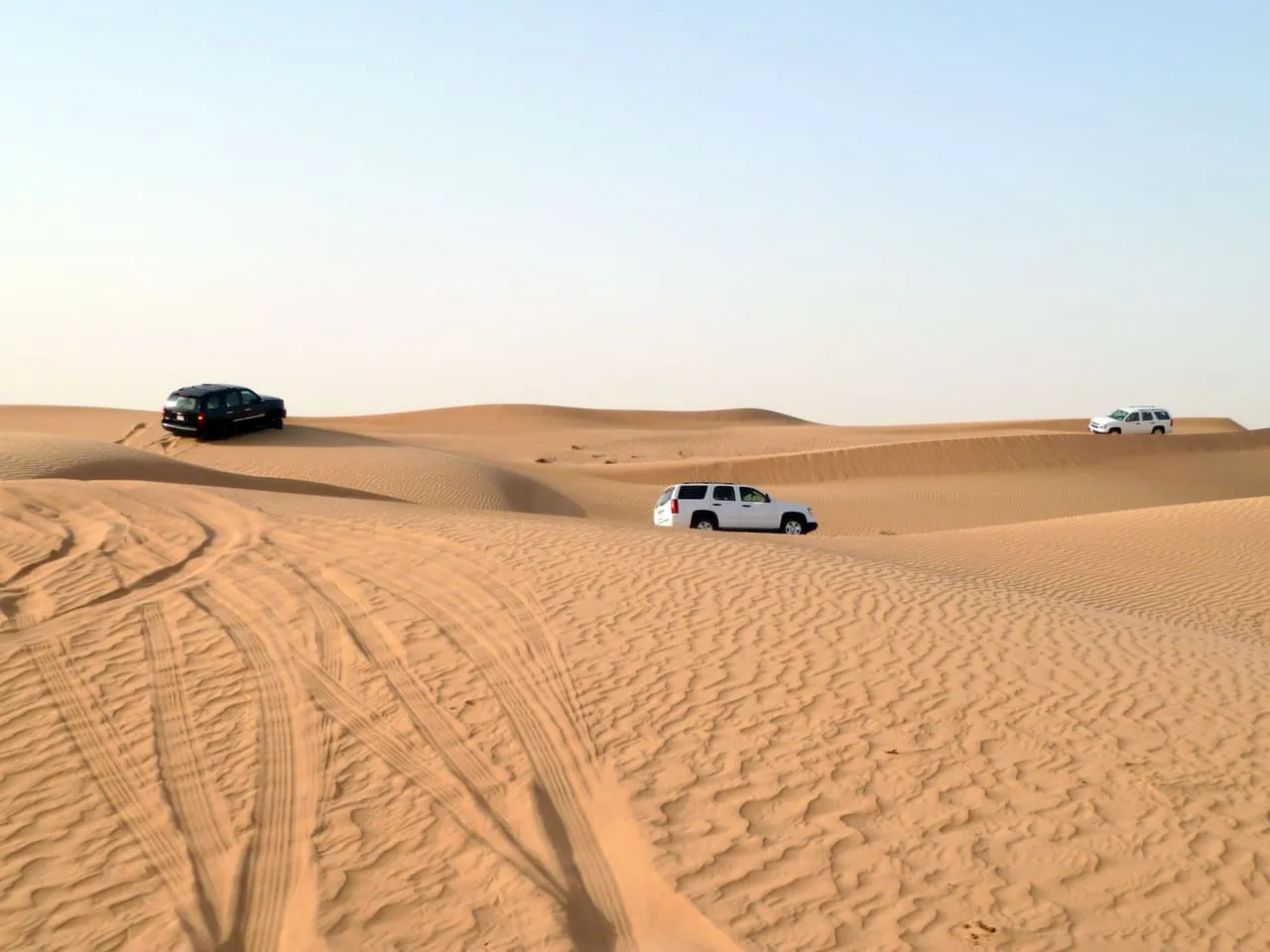 Three SUVs crossing the sand dunes on a desert safari outside Dubai, with tyre tracks in the foreground