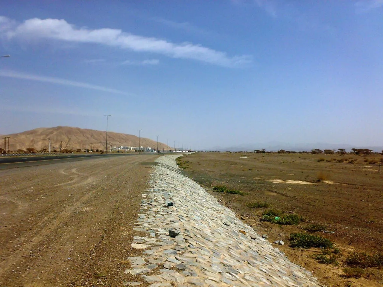 The road from Dubai to Hatta running through open desert west of Hatta, with low hills ahead