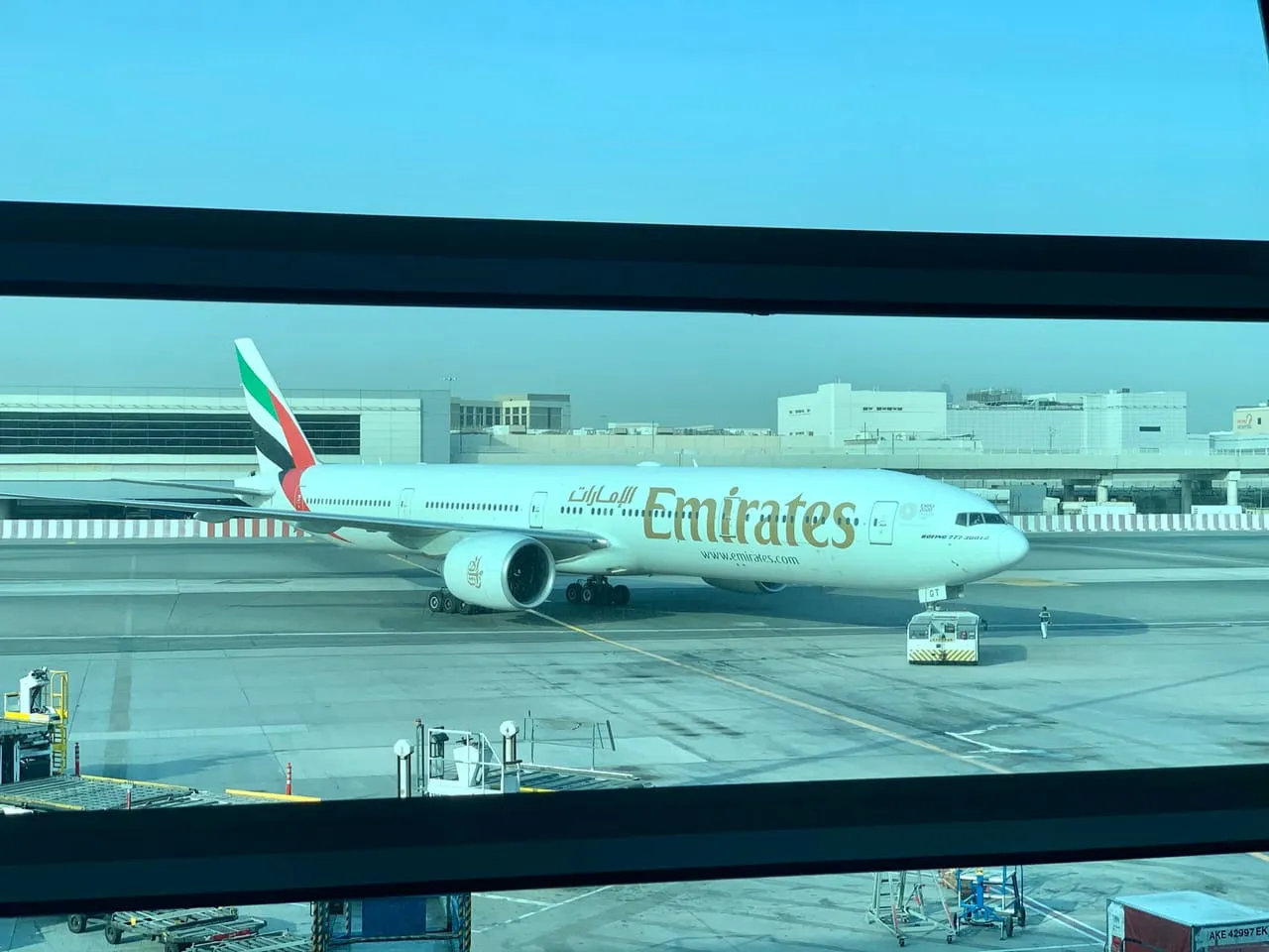 An Emirates jet at a gate, seen through the windows of Dubai International Terminal 3
