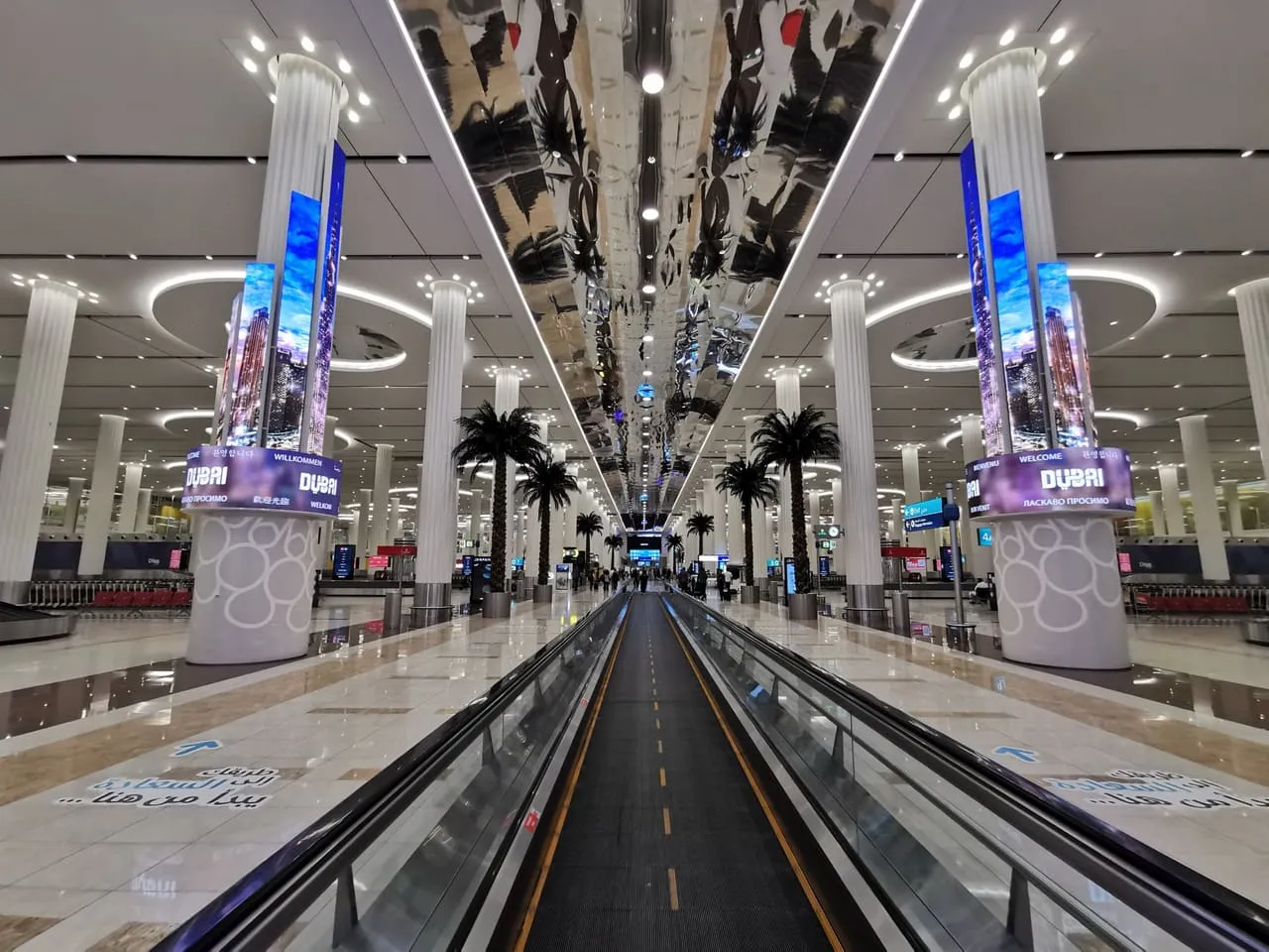 Travelator through the baggage reclaim hall at Dubai International, between screens reading Welcome to Dubai