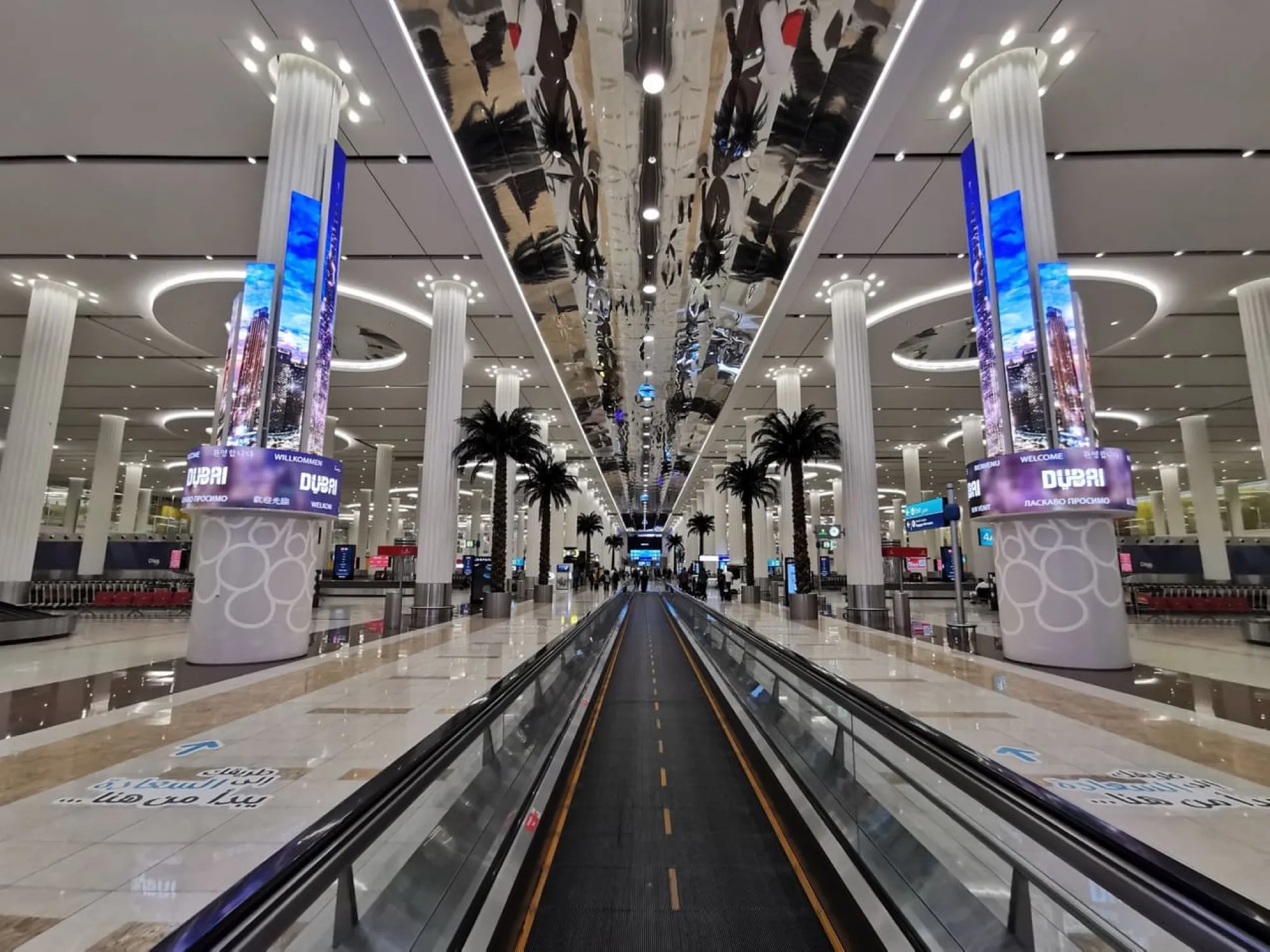 Travelator through the baggage reclaim hall at Dubai International, between screens reading Welcome to Dubai