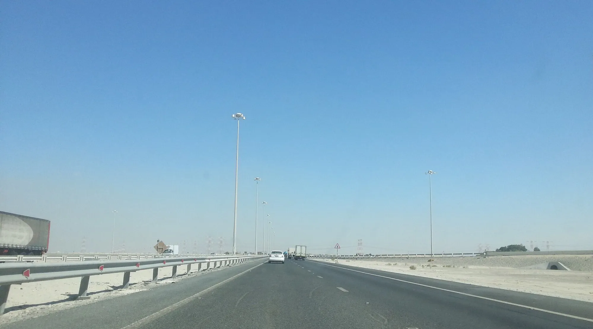 A multi-lane desert highway in western Abu Dhabi emirate with tall lighting masts and a lorry in the left lane