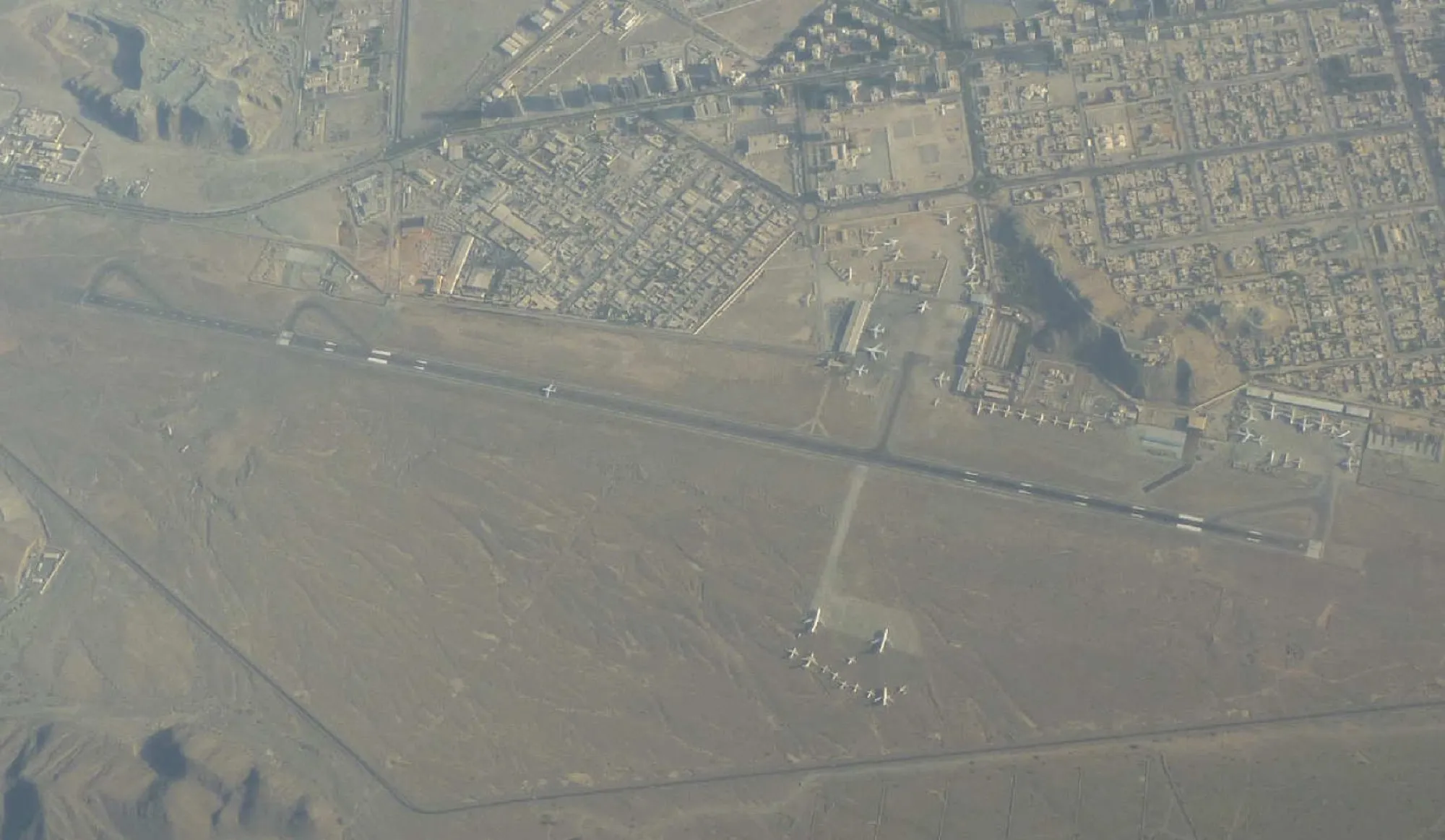 Aerial view of Fujairah International Airport, its runway beside the city with the Hajar Mountains on the left