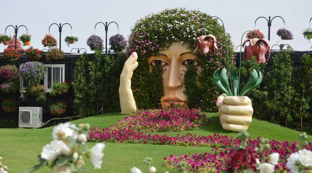 A giant face and hands sculpture covered in plants, over petunia beds at Dubai Miracle Garden