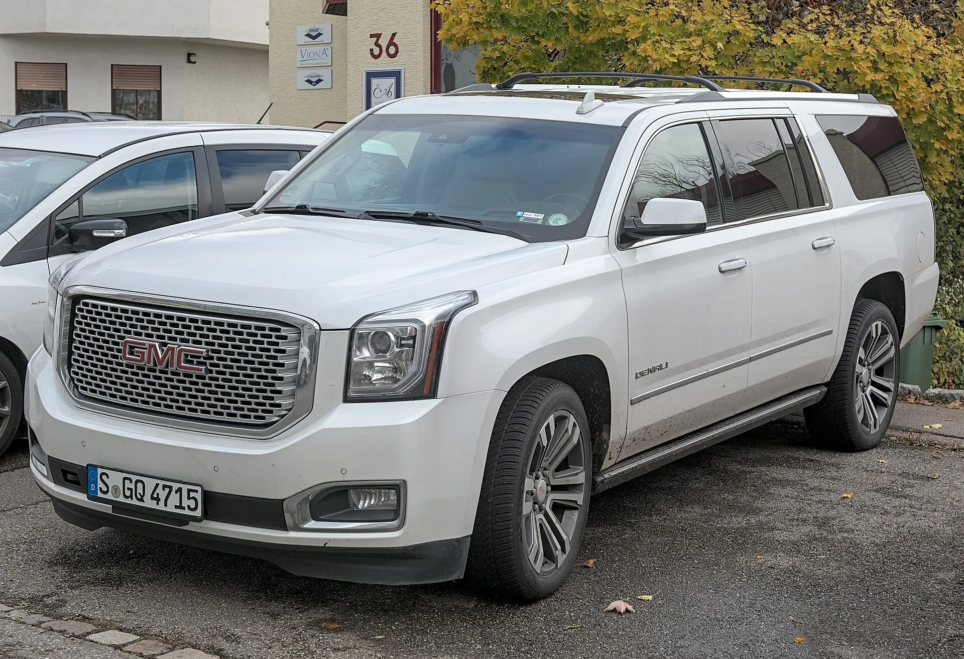A white GMC Yukon Denali three-row SUV parked at the roadside, seen from the front left