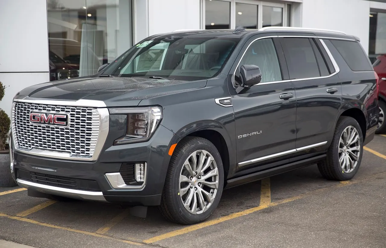 A dark grey GMC Yukon Denali SUV parked in a car park, seen from the front left