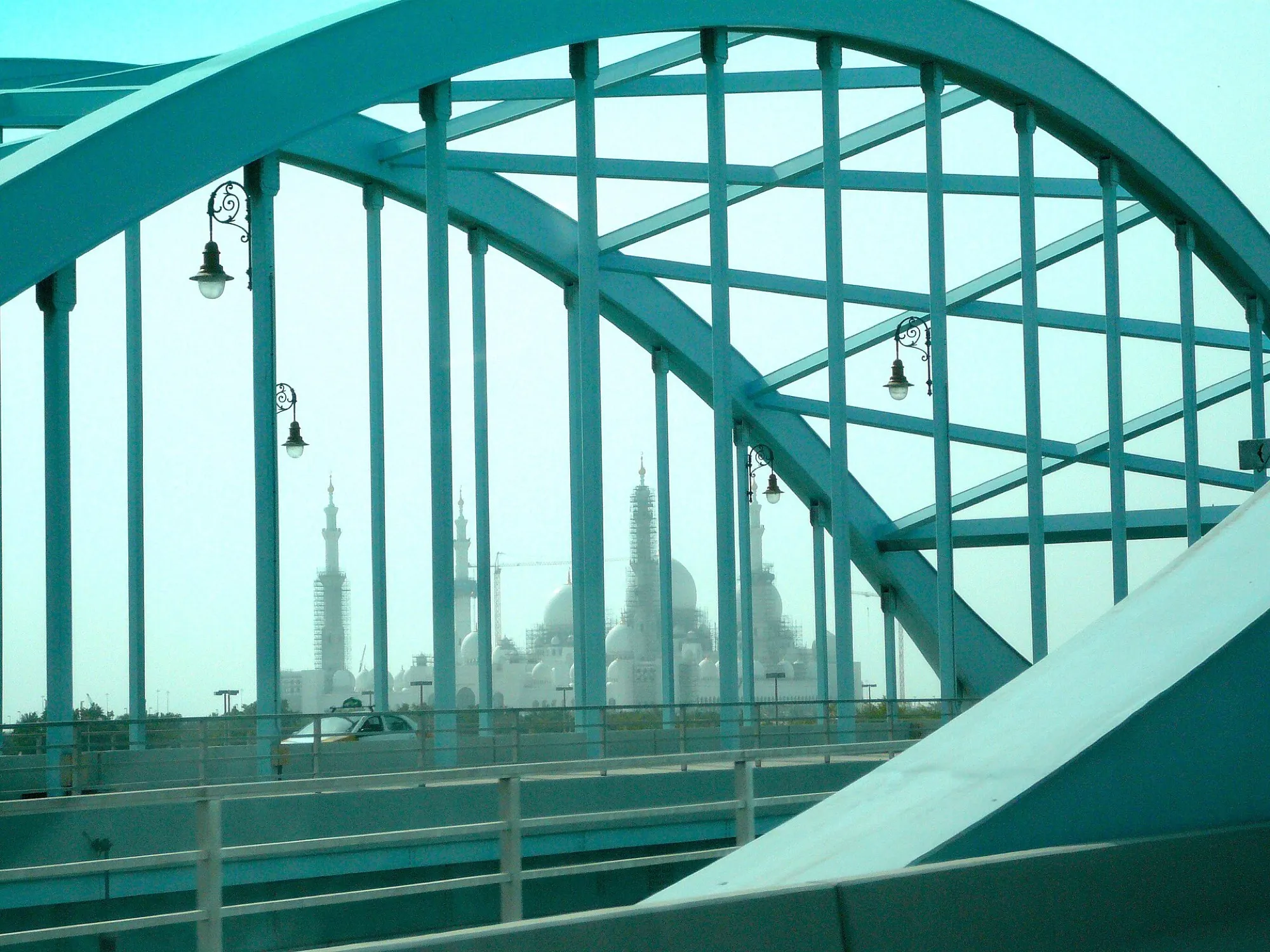The white domes and minarets of the Sheikh Zayed Grand Mosque seen through a steel bridge arch, still under construction