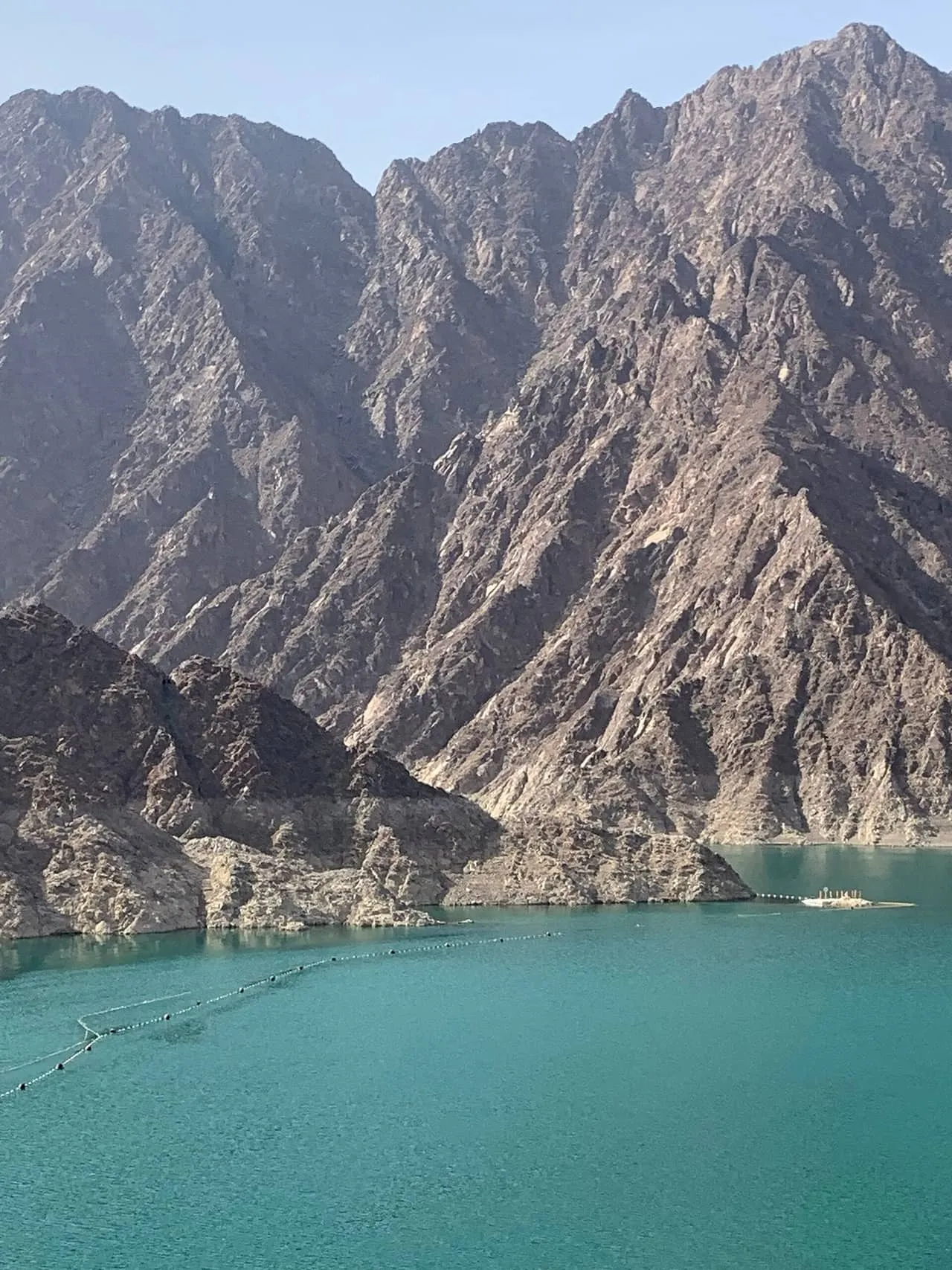 The turquoise lake behind Hatta Dam, below bare rock ridges of the Hajar Mountains