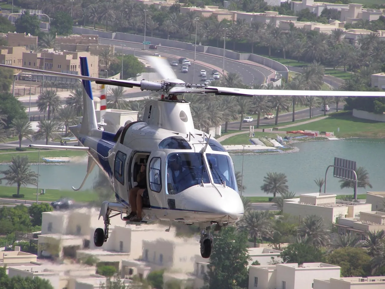 A twin-engine helicopter flying low over a palm-lined residential area of Dubai