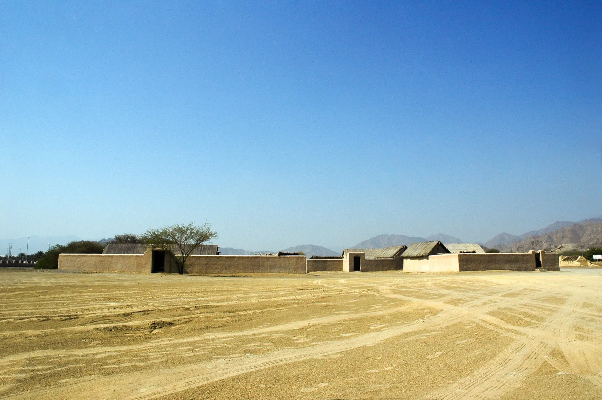 Mud-walled houses and palm-thatched roofs of the Heritage Village in Fujairah, with mountains on the horizon