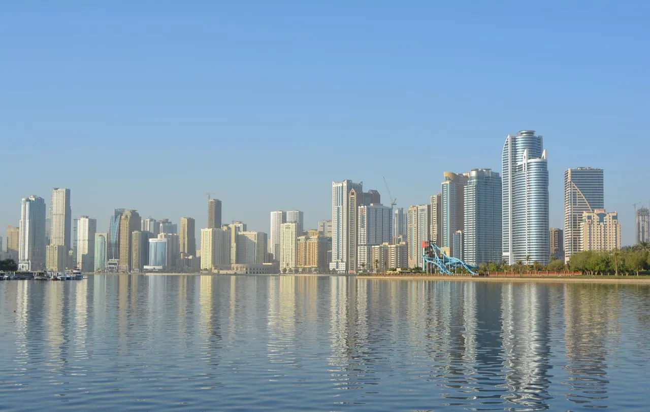 Sharjah's high-rise towers reflected in the still water of the lagoon on a clear morning