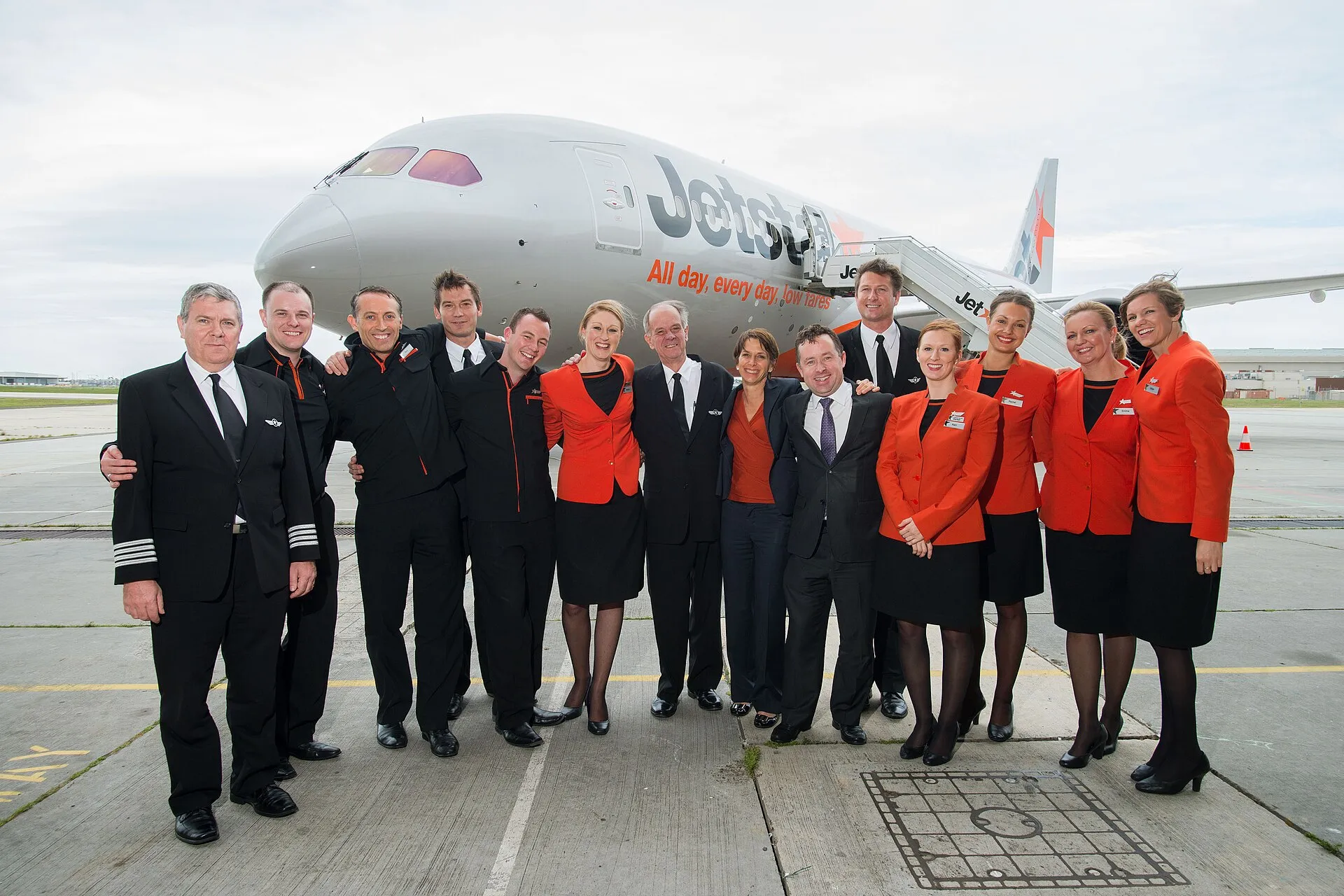 Pilots, cabin crew and two executives in uniform and suits posing together in front of a Jetstar Boeing 787 Dreamliner