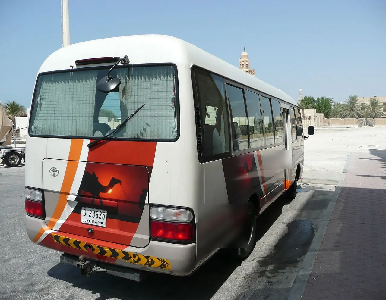 A white Toyota Coaster minibus parked at the kerb in Jumeirah, Dubai, seen from behind