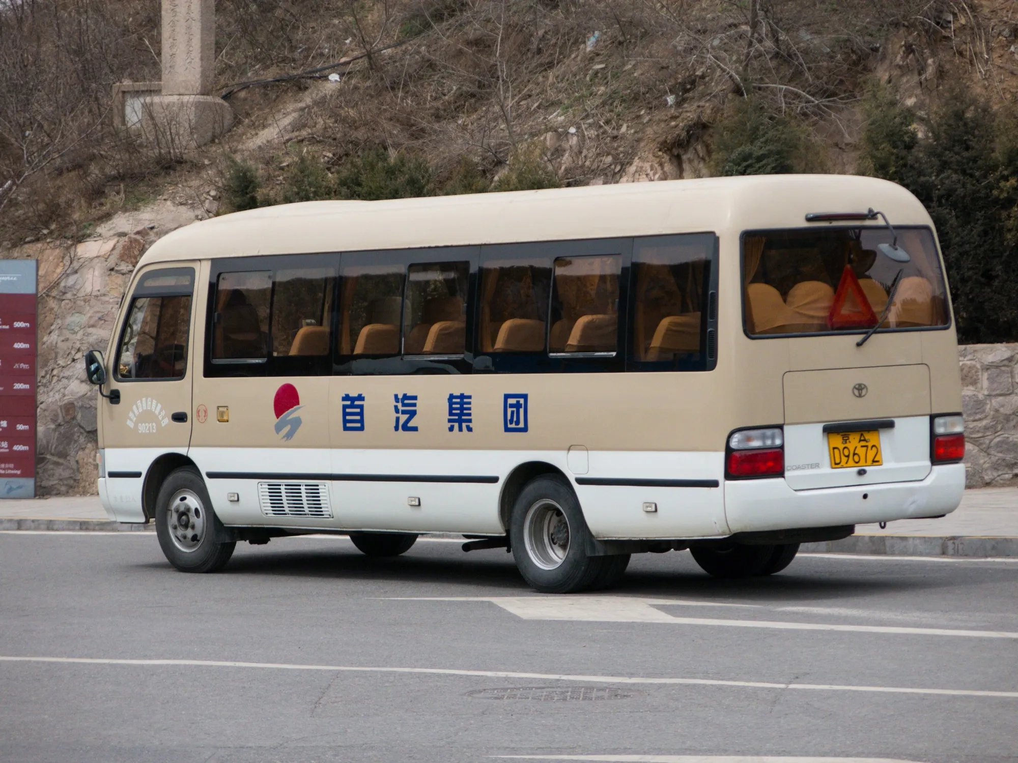 A cream and white Toyota Coaster midi bus, parked beside a road
