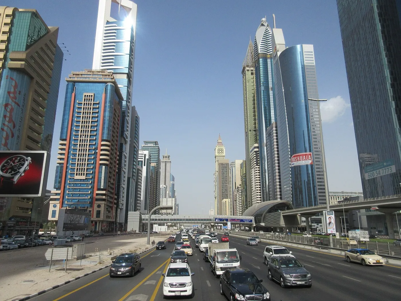 Cars on Sheikh Zayed Road in Dubai with glass towers on both sides and a metro station building on the right