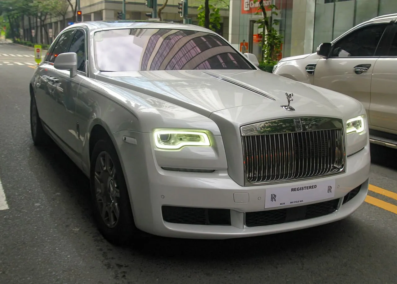 A white Rolls-Royce Ghost sedan seen from the front, parked on a city street