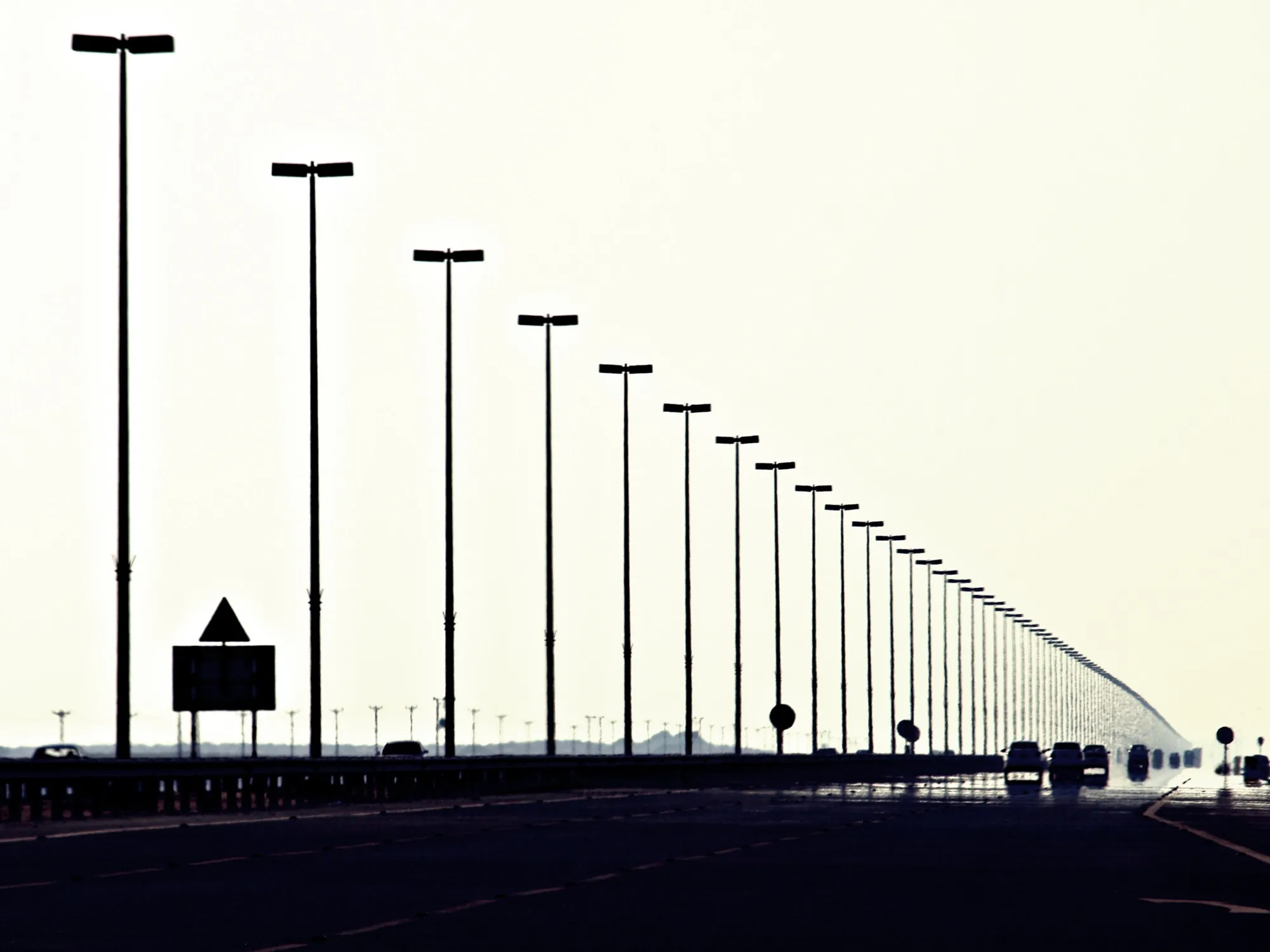 Tall lamp posts lining the Dubai to Abu Dhabi freeway, with traffic silhouetted against a pale sky