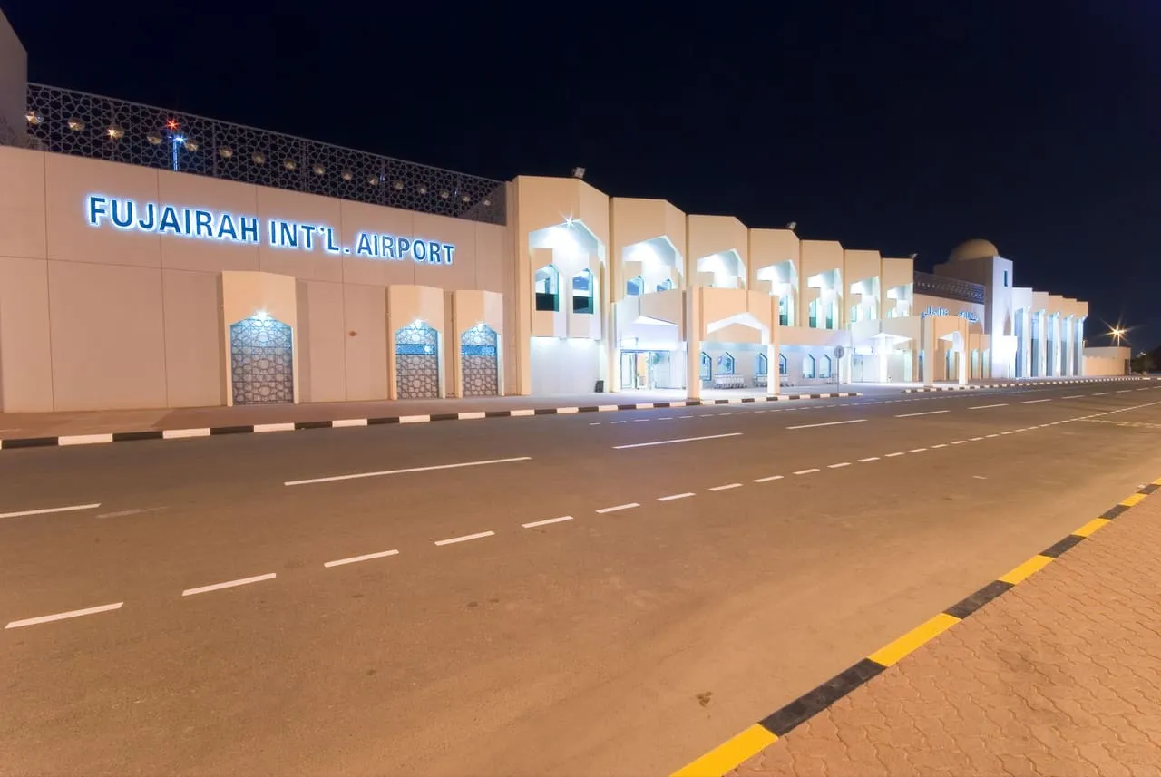 The front of the Fujairah International Airport terminal lit up at night, with the airport's name in blue letters