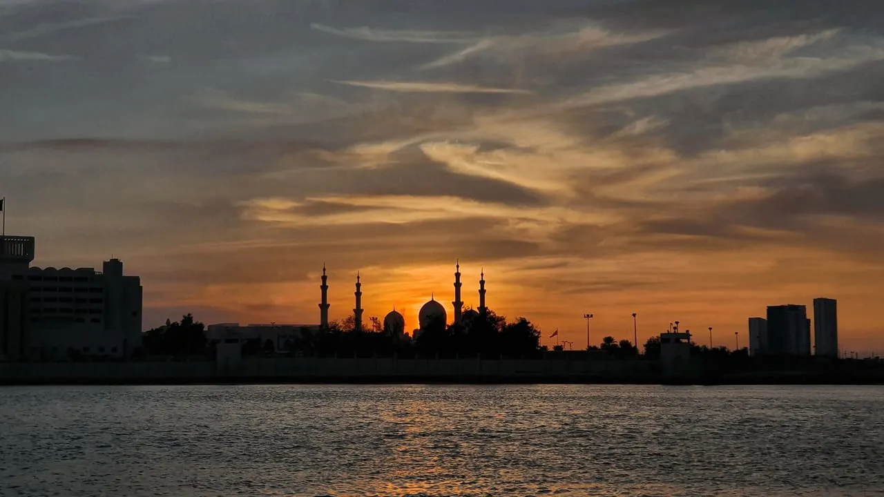 The domes and minarets of the Sheikh Zayed Grand Mosque in silhouette at sunset, seen across the water in Abu Dhabi